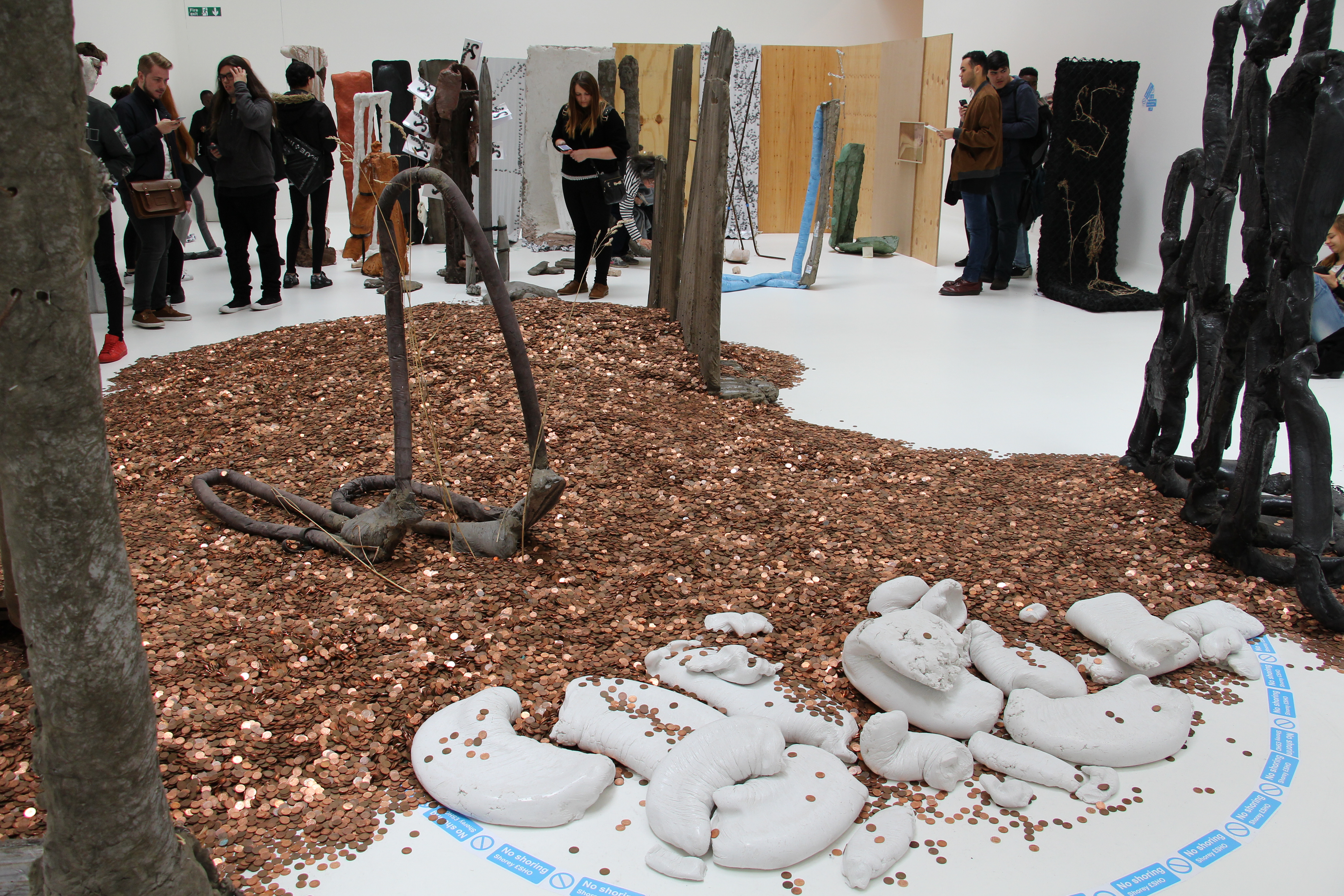 Several people can be seen admiring a group of artworks, including sculptures and thousands of pennies on the ground.