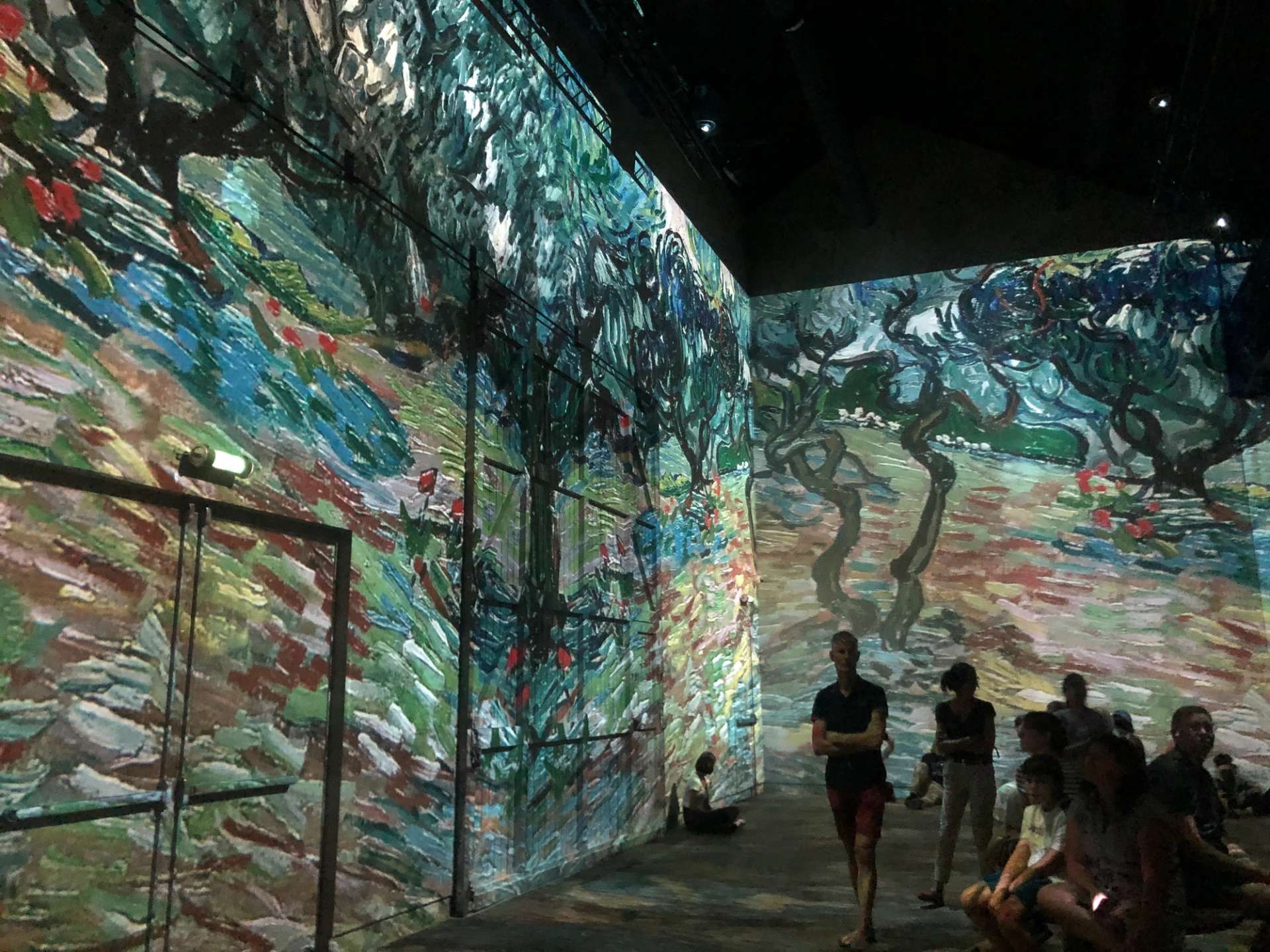 This photograph shows Vincent Van Gogh's art projected in large-scale in a room, as people walk around it.
