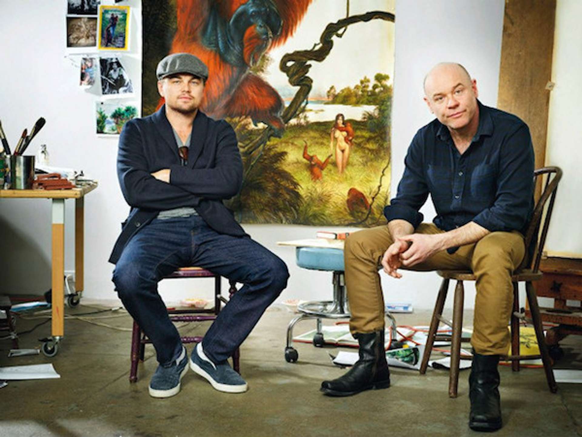 Actor Leonardo DiCaprio and artist Walton Ford sitting in the artist's studio, with a painting behind them.