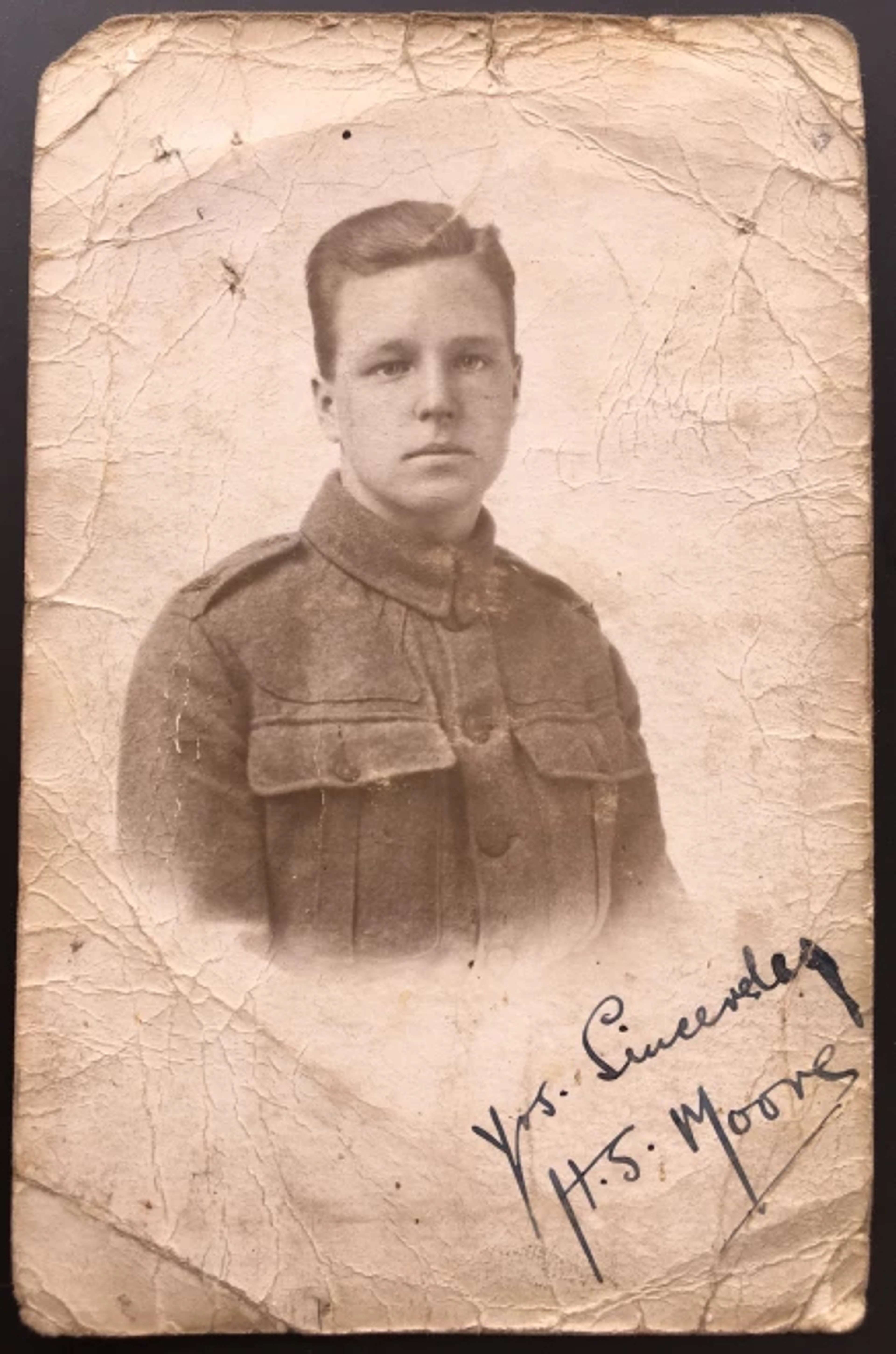 A vignette of a young man in military uniform on crinkled paper. The young man, identified as Henry Moore with combed-over hair and a stoic facial expression, is depicted within the circular crop. In the lower right-hand corner, the vignette is signed with the initials 'H.S. Moore'.