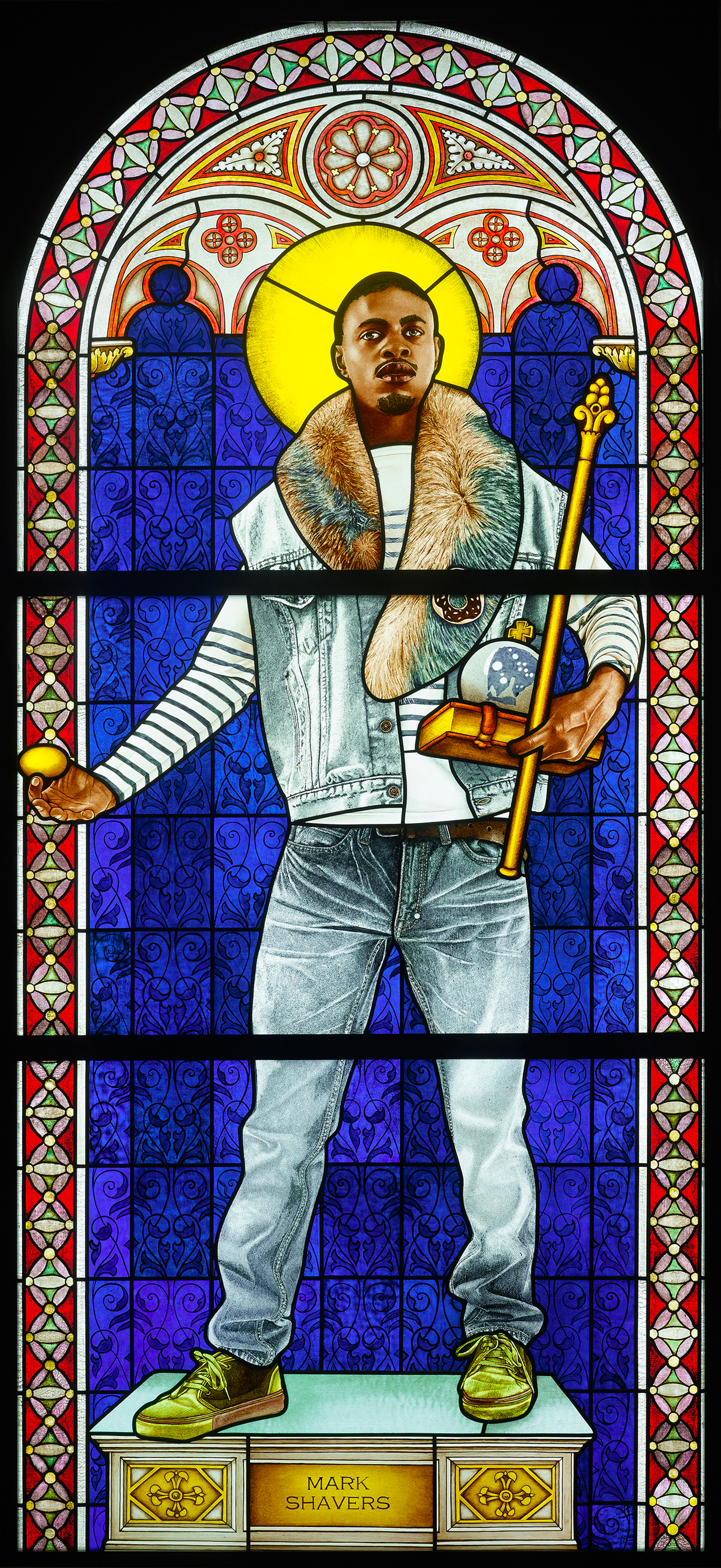 A triptych-style artwork, designed to resemble a stained glass altarpiece, portrays a black man standing on a raised platform in the middle panel. The platform is embellished with a gold plaque. The man is casually dressed, wearing denim jeans, a denim vest, and a blue long-sleeve striped shirt underneath. The background behind him is navy blue, with a golden circle positioned behind his head. The artwork is adorned with intricate red and green borders.