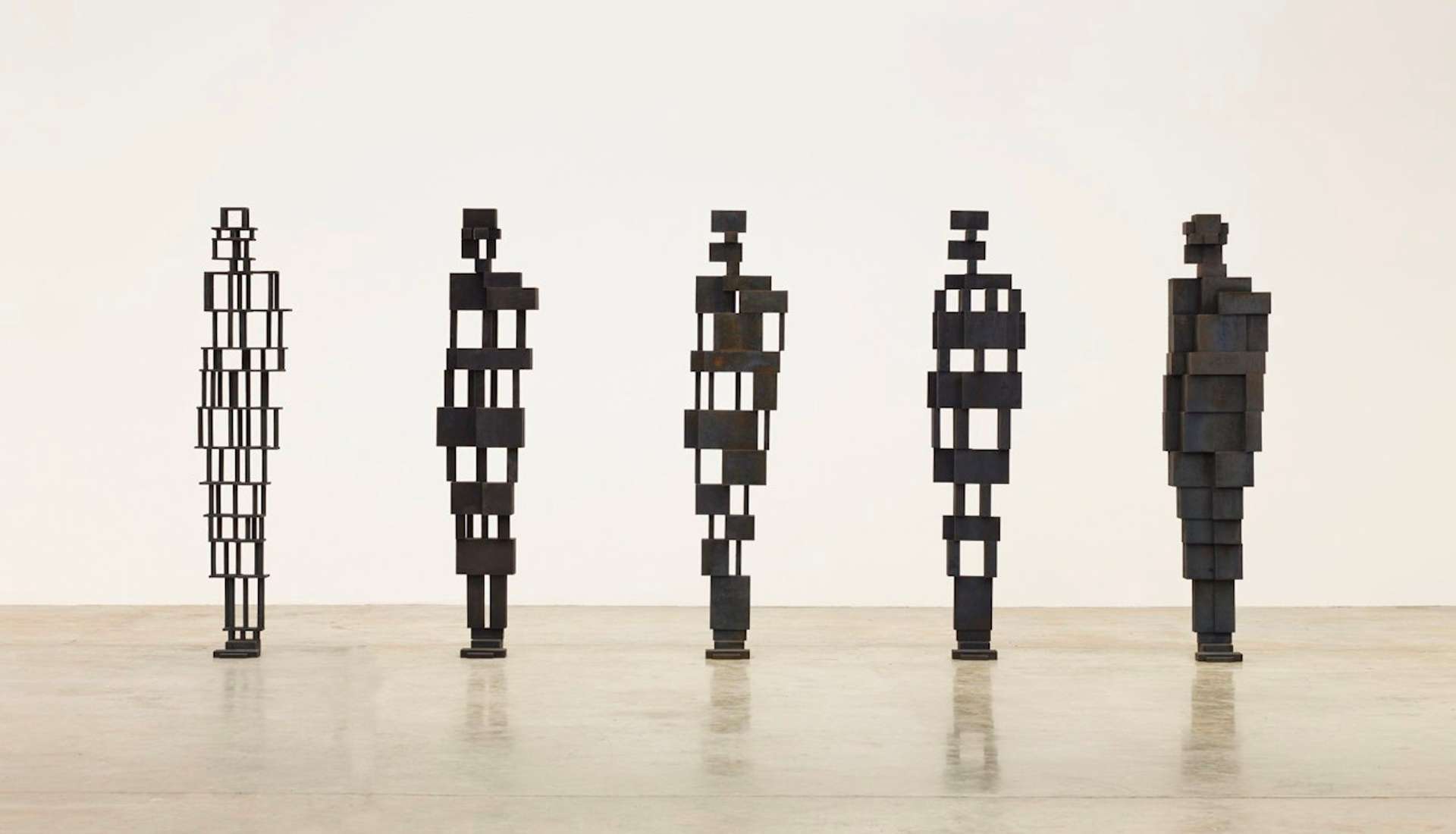 Five freestanding sculptures depicting the essence of the human form, void of specific defining characteristics. Each sculpture is crafted using different materials, ranging from sparsely interwoven elements to more densely filled volumes, creating varying degrees of texture and composition. The sculptures are photographed in an empty gallery space, showcasing their unique forms and materiality.