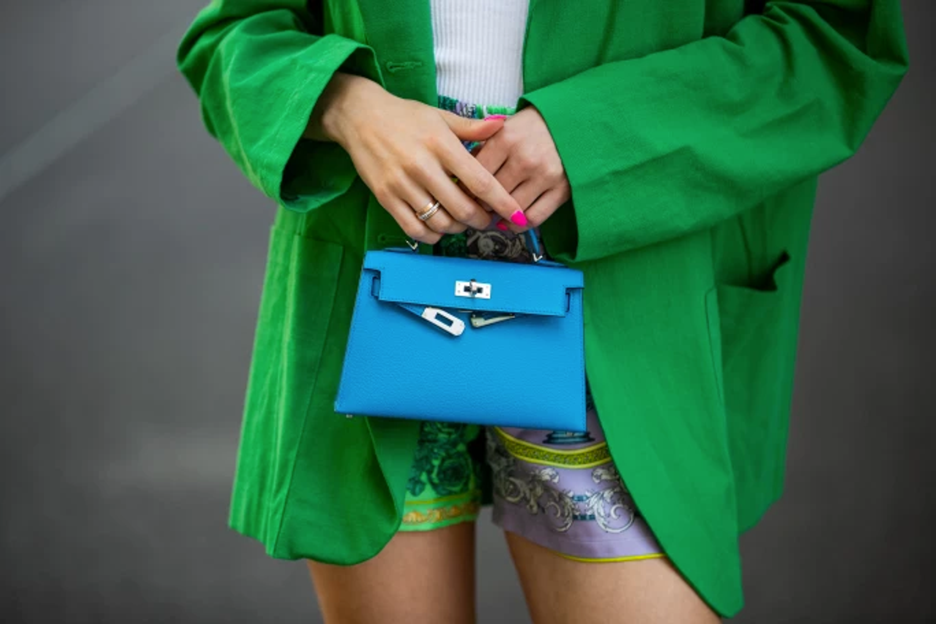 Close up of a woman in a green coat holding a small, blue Hermès handbag