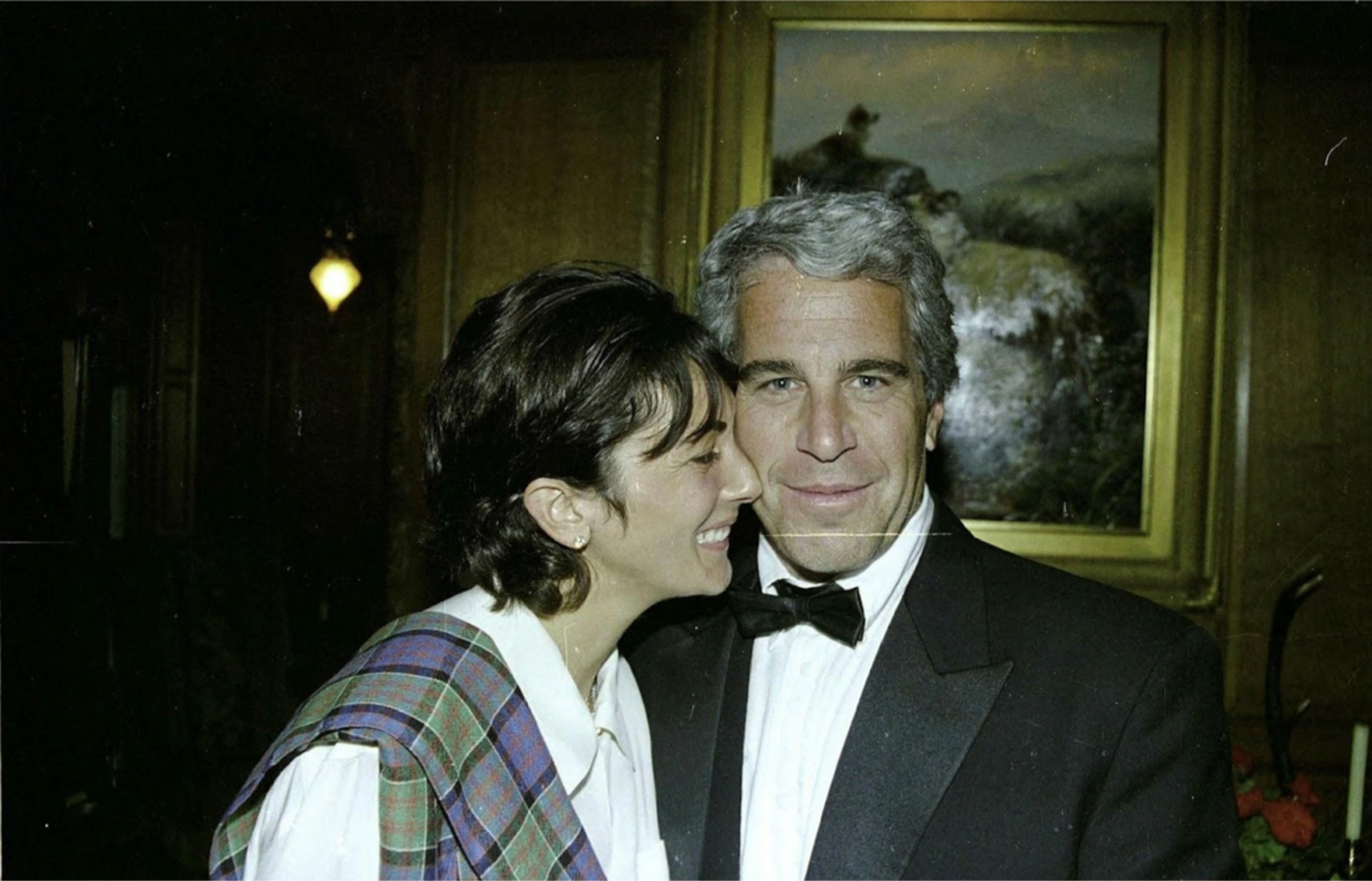 Ghislaine Maxwell and Jeffrey Epstein embracing in front of an oil painting.