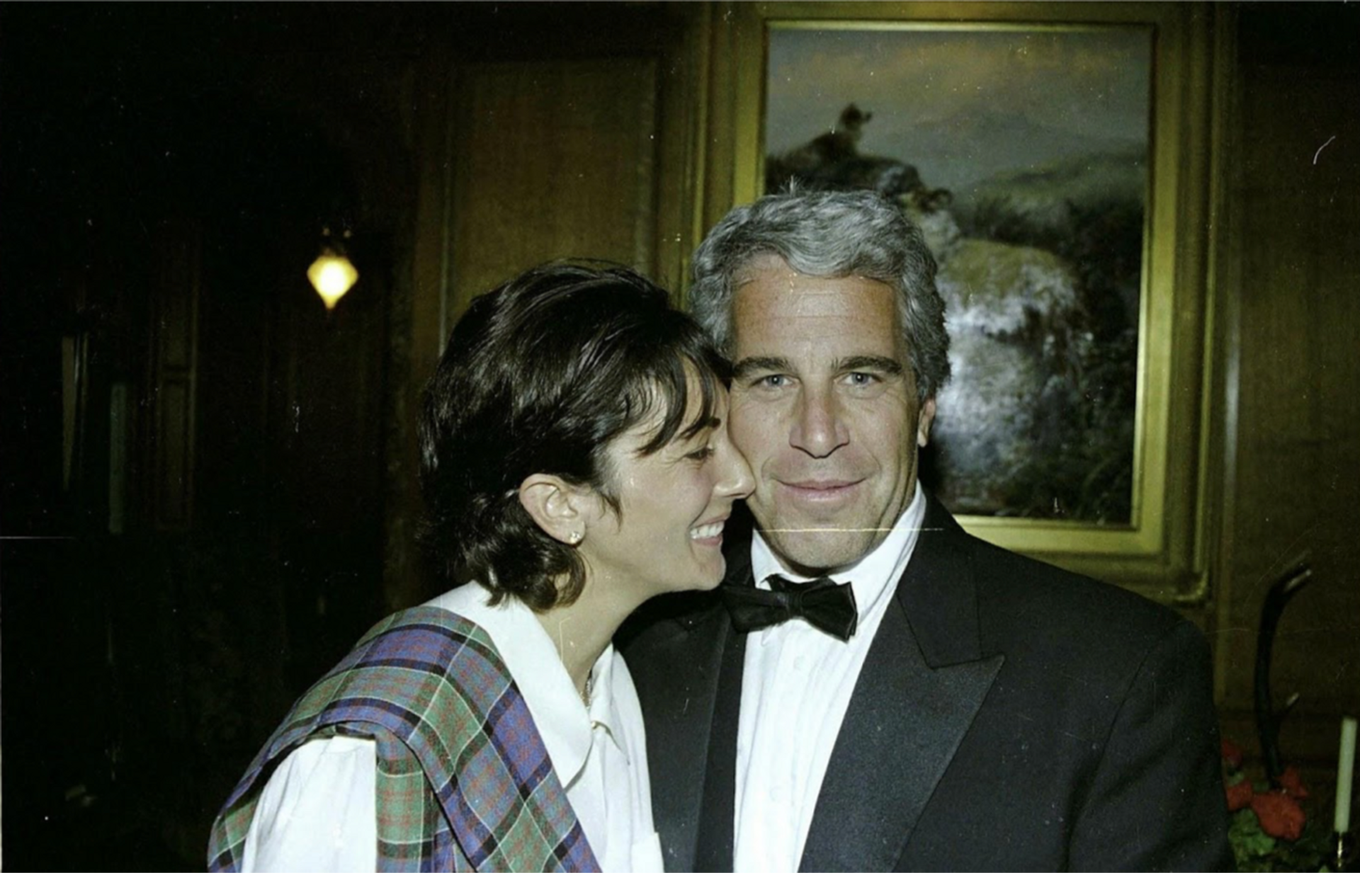 Ghislaine Maxwell and Jeffrey Epstein embracing in front of an oil painting.
