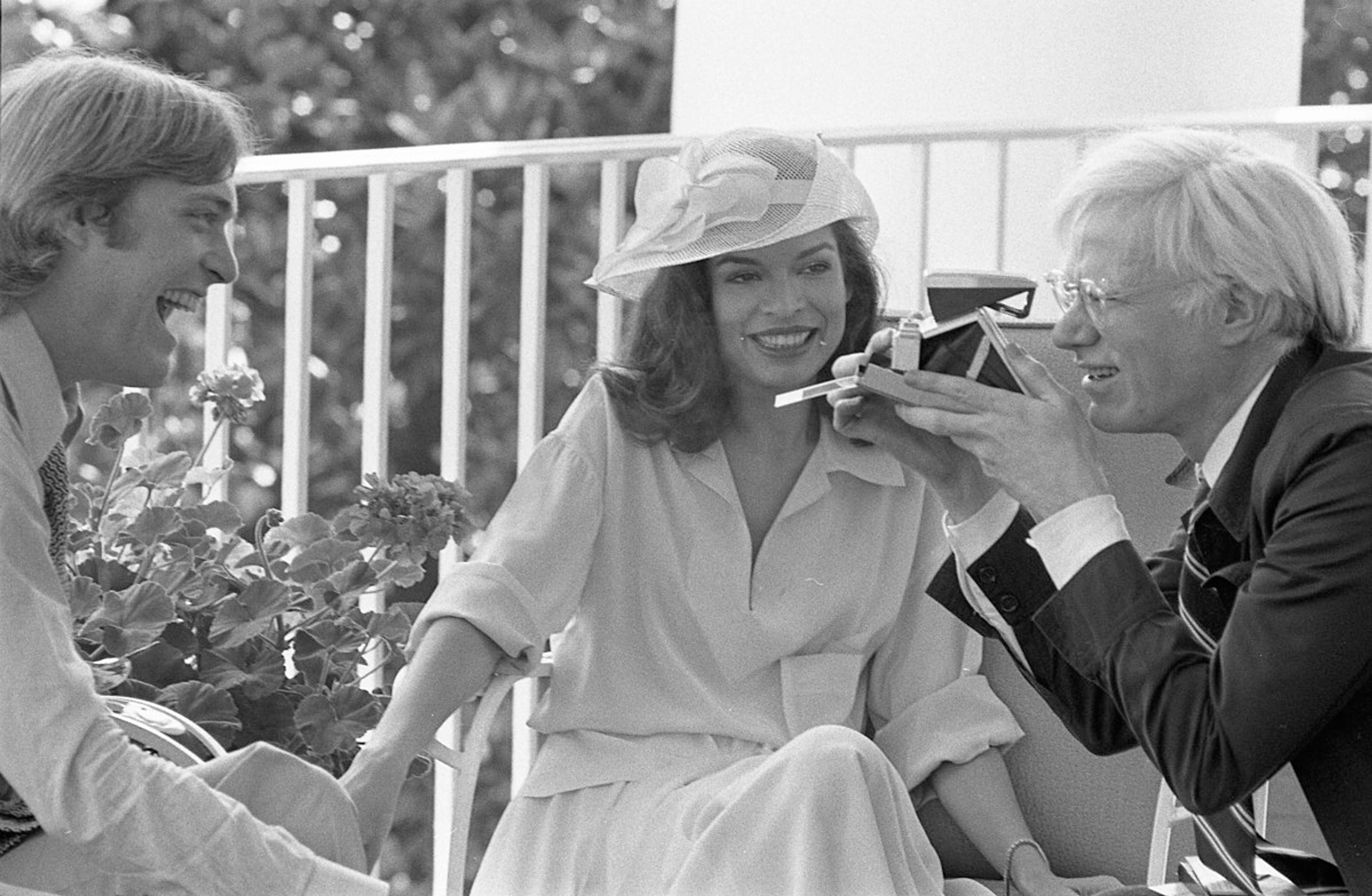 Photograph of Andy Warhol Taking a Polaroid Picture while Sitting with Jack Ford and Bianca Jagger on the Truman Balcony