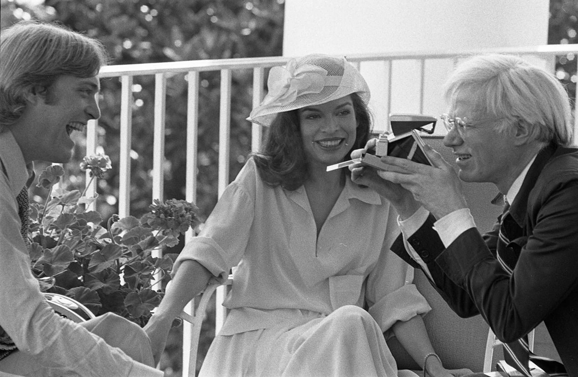 Photograph of Andy Warhol Taking a Polaroid Picture while Sitting with Jack Ford and Bianca Jagger on the Truman Balcony