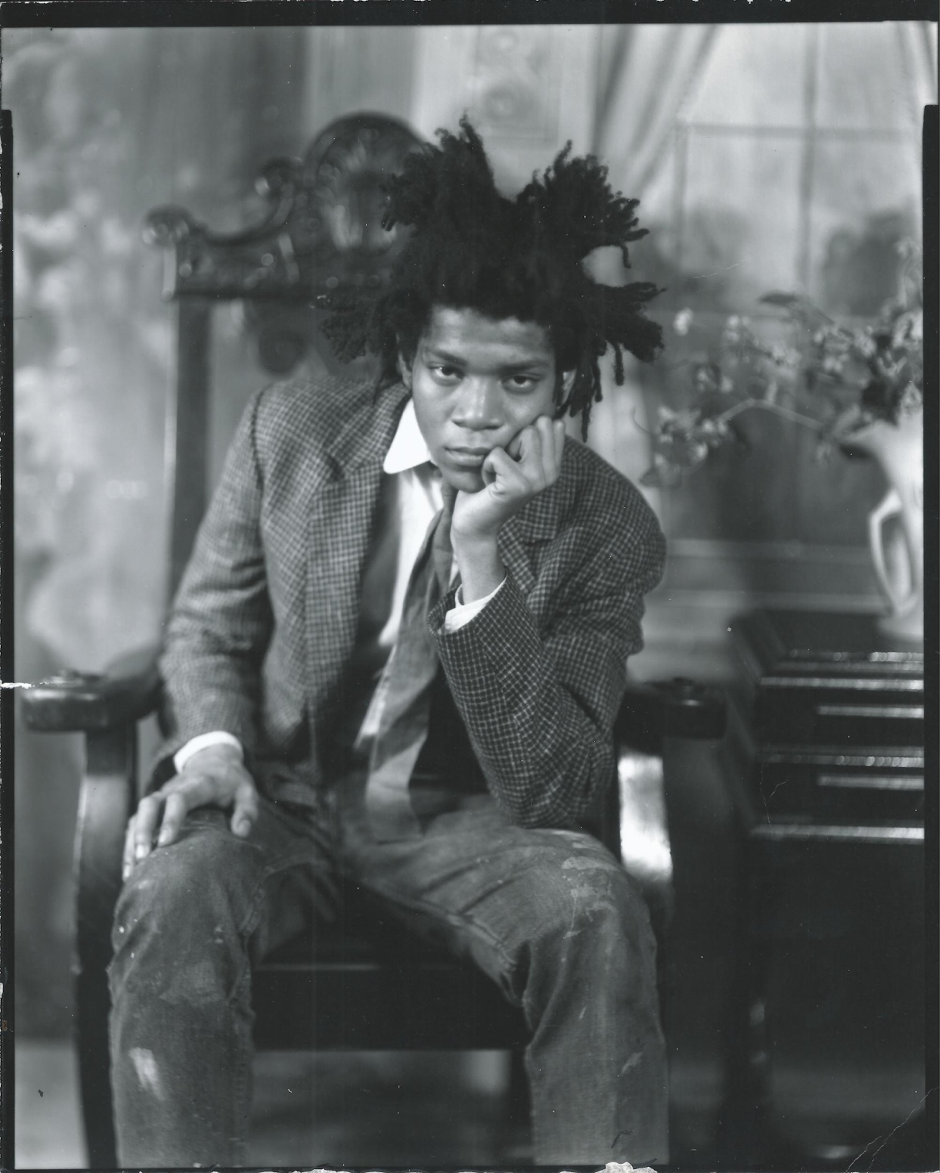 Black and white photograph of Jean-Michel Basquiat sitting on a chair.
