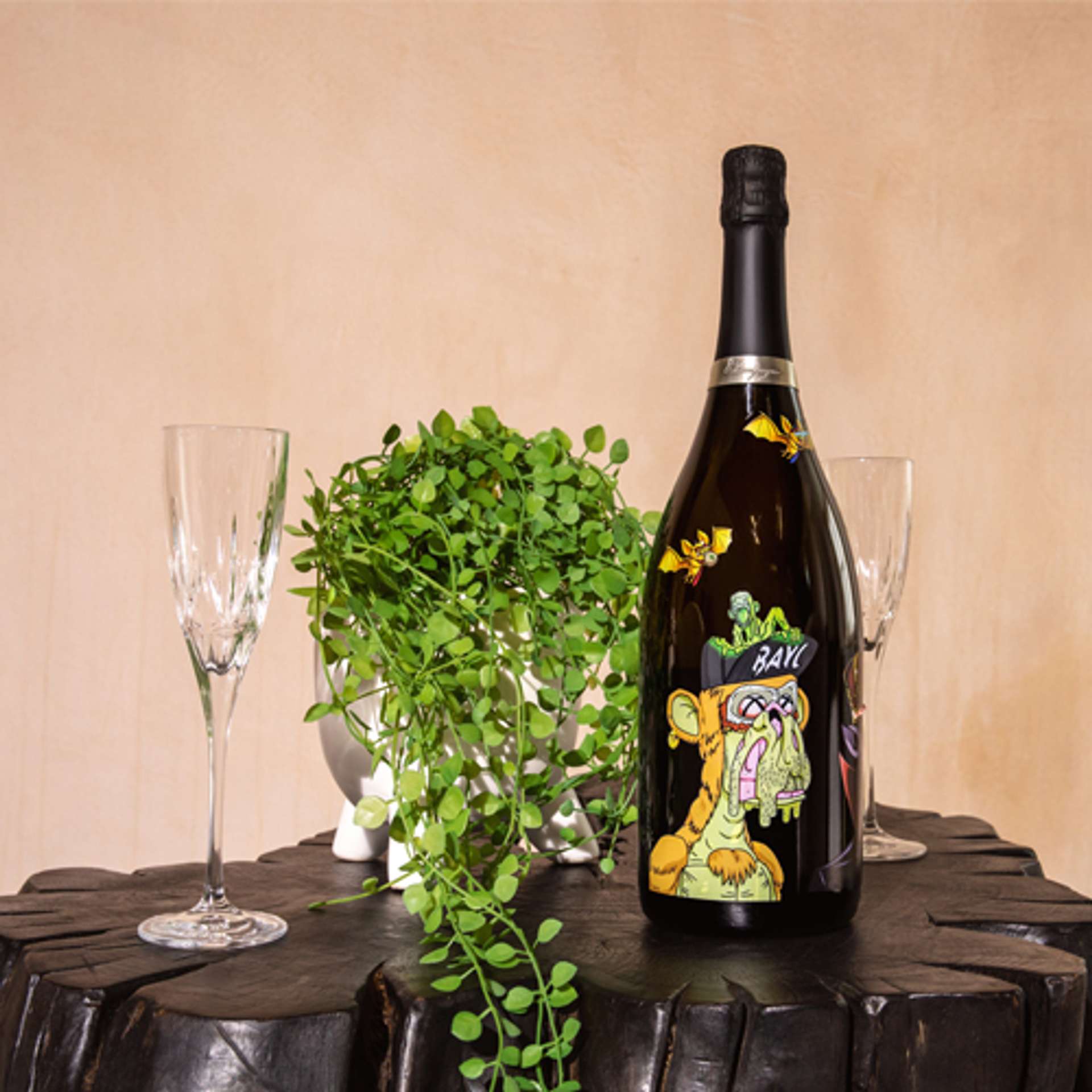 A black wine bottle with a yellow graphic ape, two glasses and a green plant on top of a black wooden side table