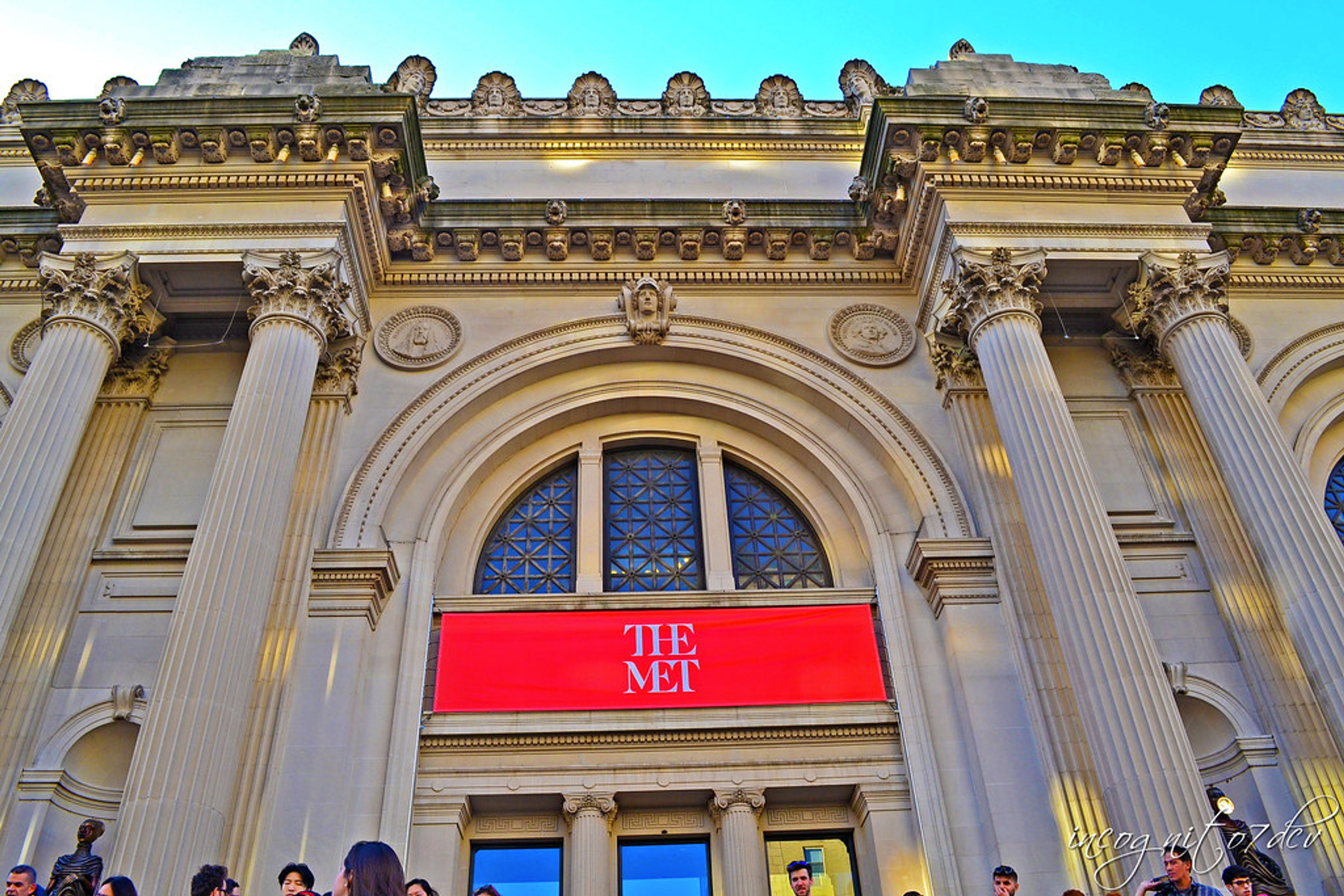 An image of the facade of the Metropolitan Museum of Art, adorned with a red banner with the museum's logo.