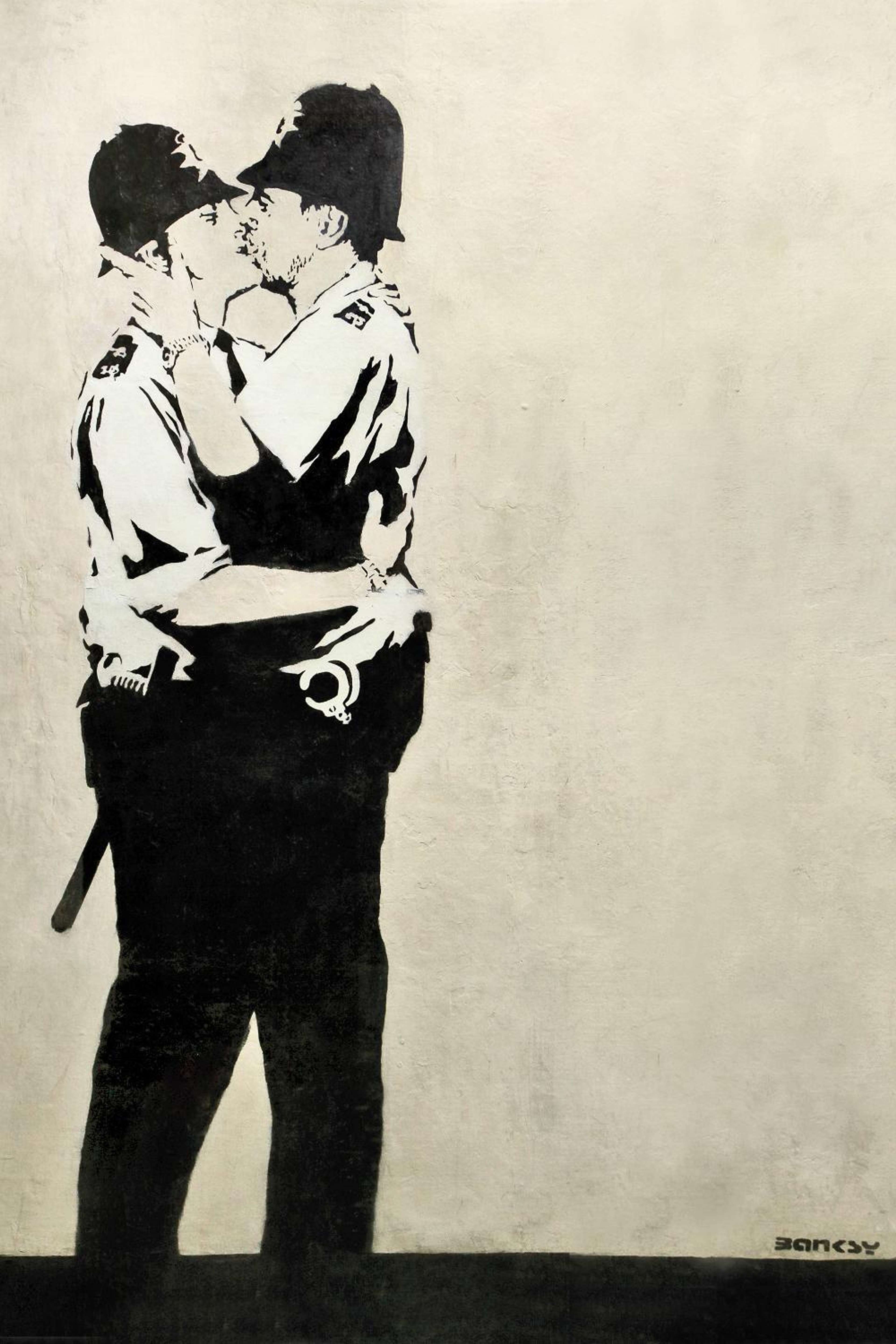 A black-and-white stencil mural of two uniformed British policemen in custodian helmets kissing, painted large on a building wall.