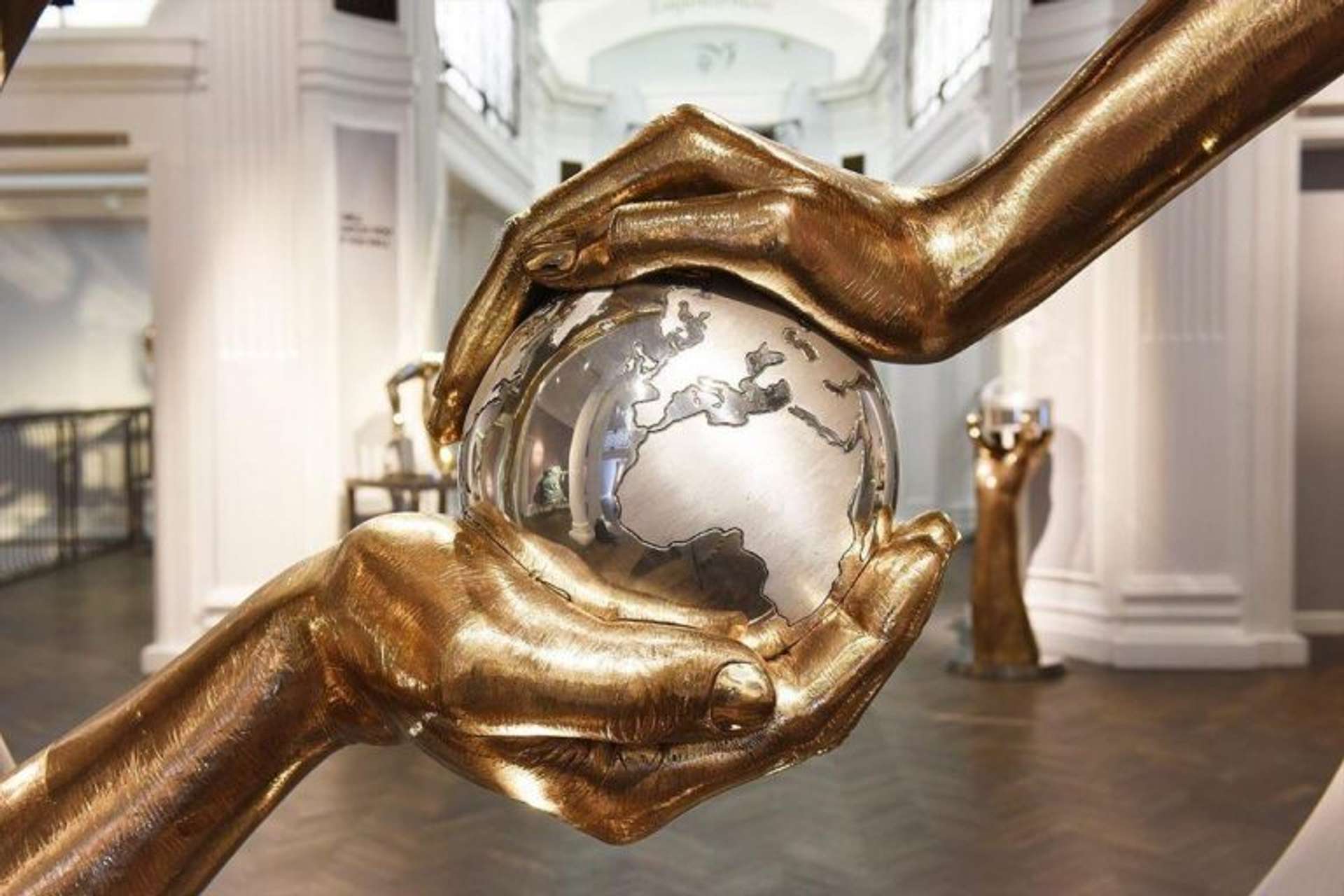 A sculpture titled "Empowerment" featuring two oversized hands emerging from a block of marble or stone, one hand supporting the other in a gesture of strength and support.