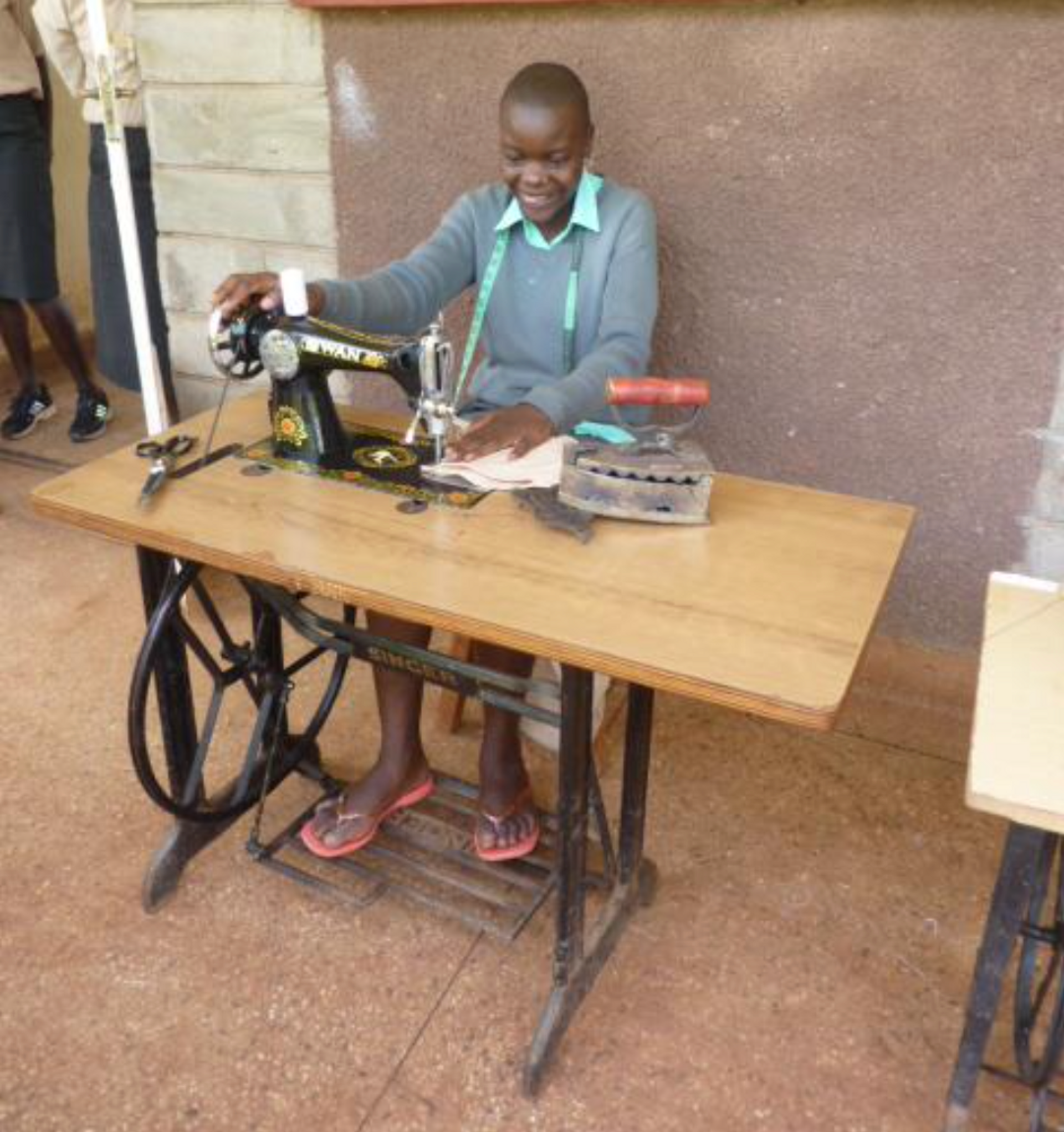 Damaris came to W.O.R.K. as a teenager and was not eligible for Secondary school. W.O.R.K. placed her in a Vocational Training Centre where she completed a National Certificate in Tailoring and Dressmaking. Here she is with the Sewing machine (provided by W.O.R.K.) and she runs her own successful business and is doing well. You can also see the Iron she uses – it works when filled by hot charcoal - no electricity is available!