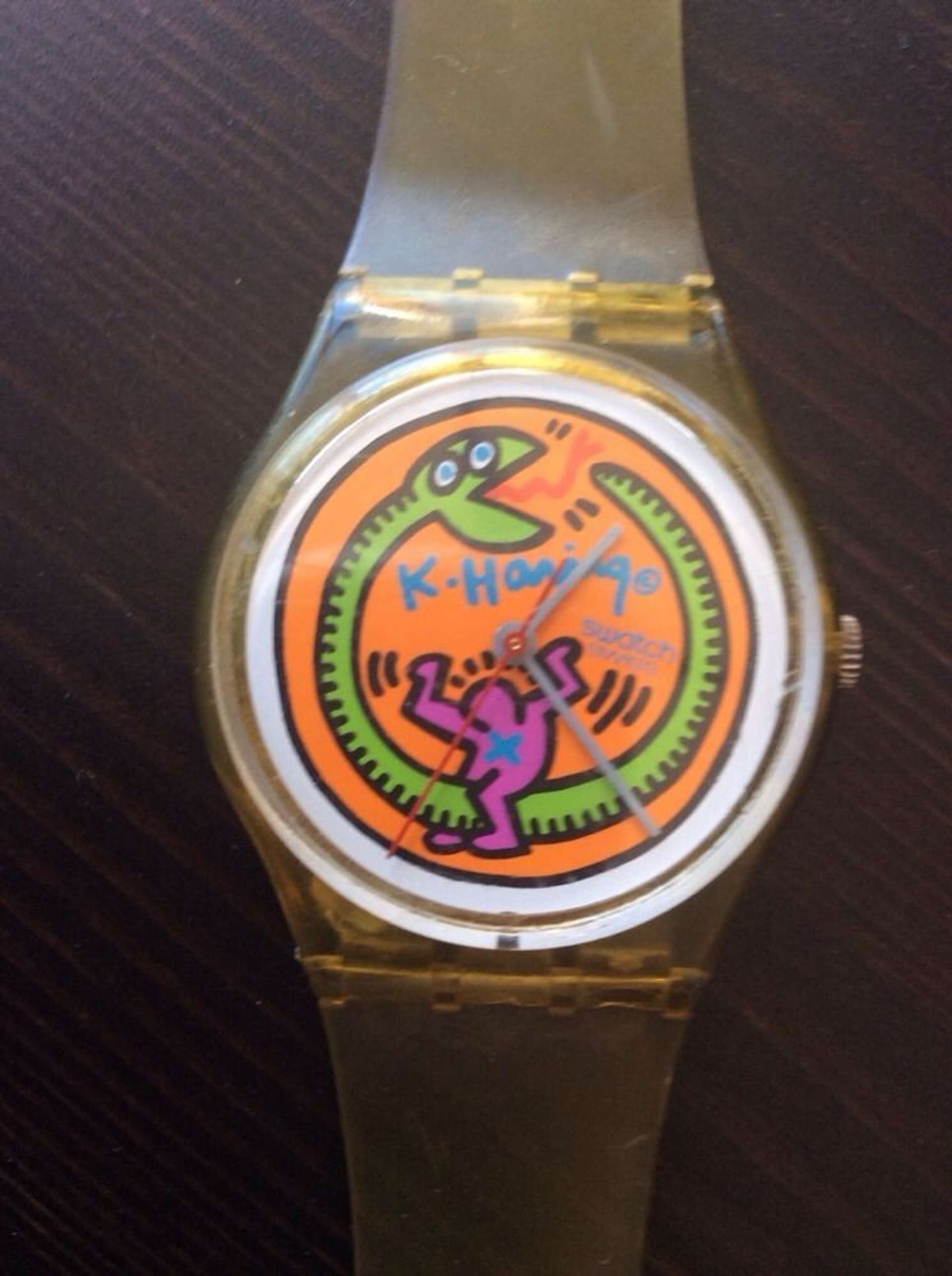 A Swatch watch with a design by Keith Haring on the watch face, showing a small purple figure on a green snake