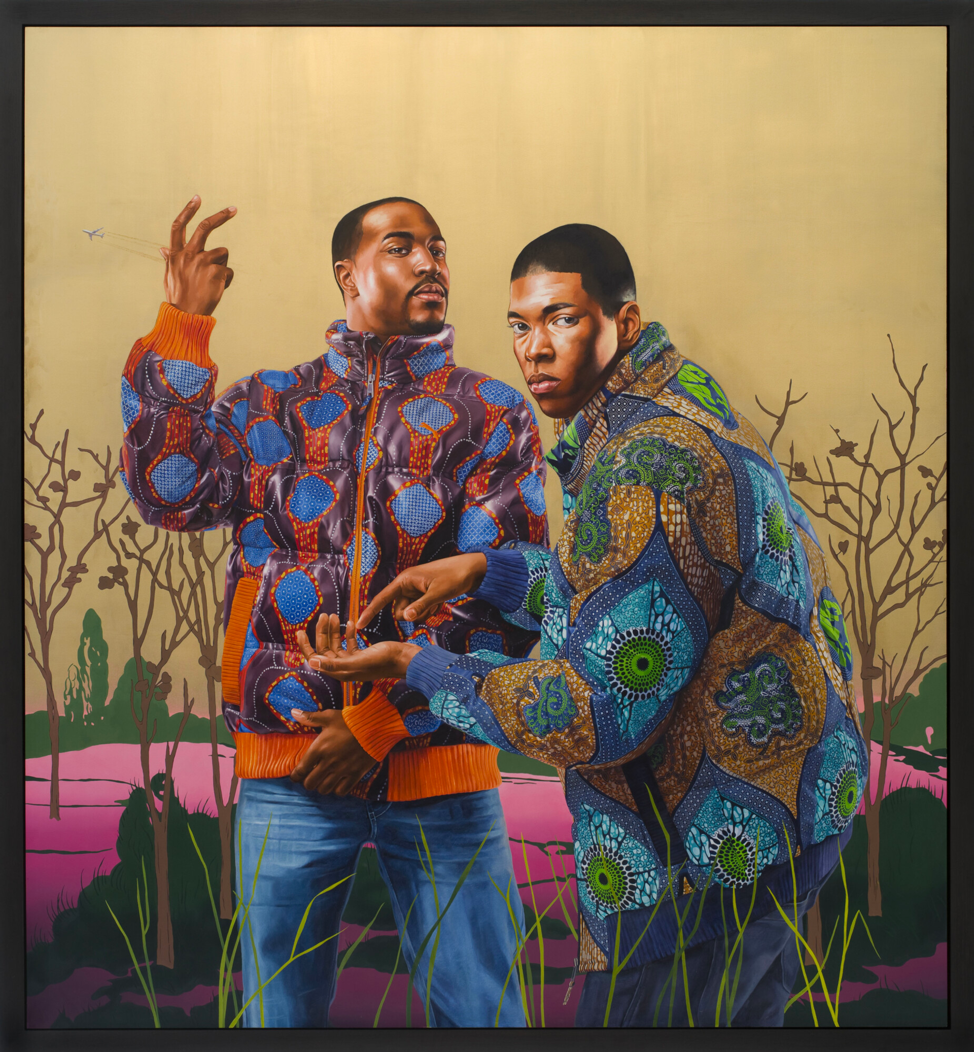 Two black men in jeans and vibrant oriental patterned zip-up jackets. One man poses with his hand near his crotch while the other raises his hand in a performance stance. The second man gestures with one hand and points to his palm with the other, facing the viewer. The scene is set outdoors with a golden sky, a pink path, and lush green bushes.