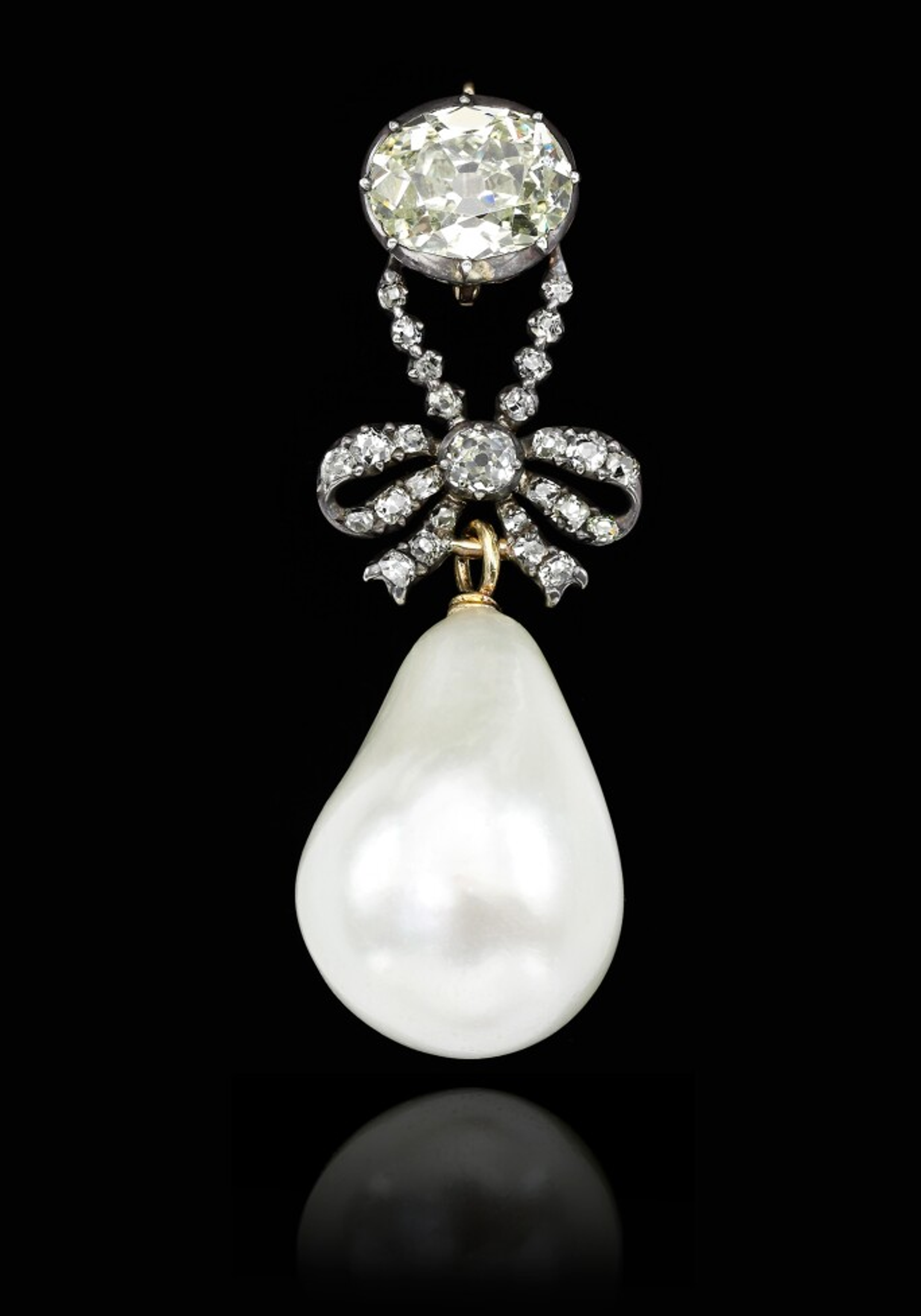 An image of a jewel worn by Queen Marie Antoinette: a large diamond bow hanging from a large diamond solitaire. A big pale pearl hangs from underneath the bow.