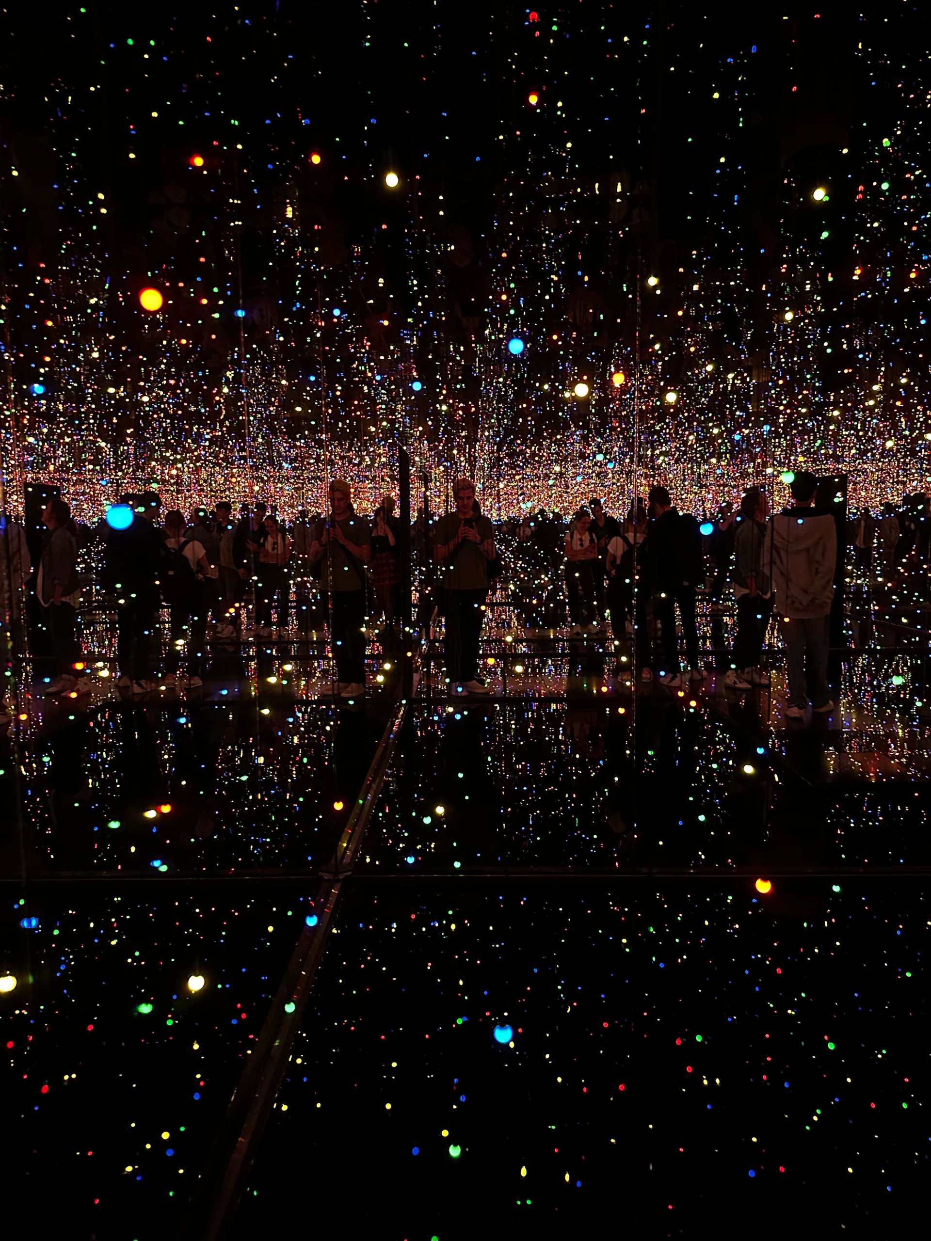 This photograph shows one of Yayoi Kusama's Infinity Rooms at the Tate Modern 2023, a mirrored environment with thousands of bright coloured lights.