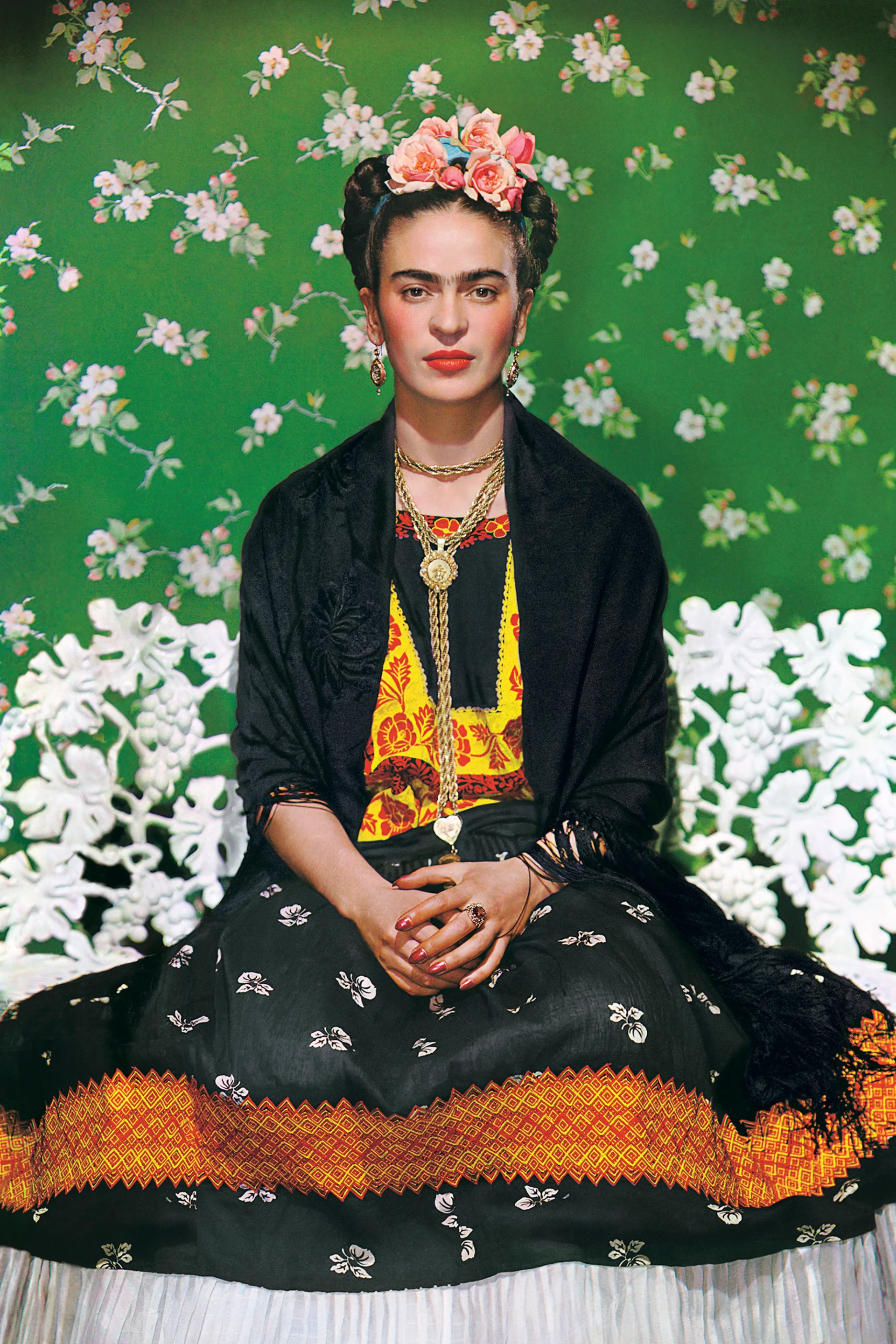 This image shows the artist Frida Kahlo against a bright green wall, staring defiantly at the camera as she is dressed in traditional Mexican attire.