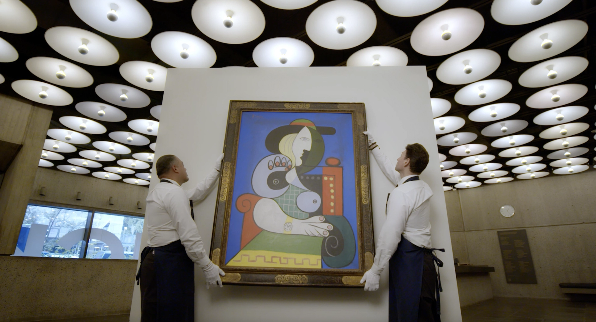 Two men are shown hanging up Picasso's work on a white wall.