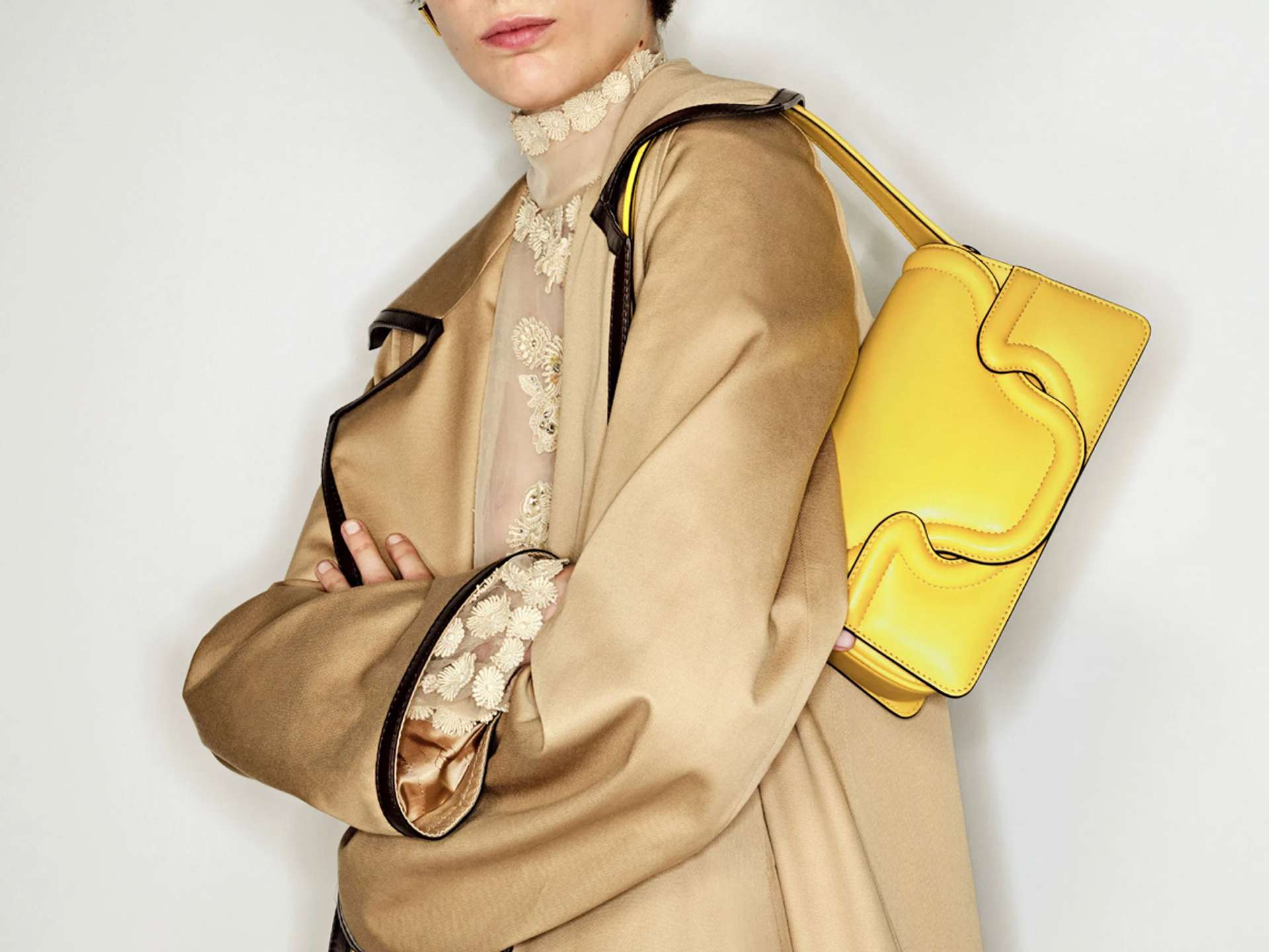 Woman wearing a camel trench coat and bright yellow shoulder bag over her shoulder
