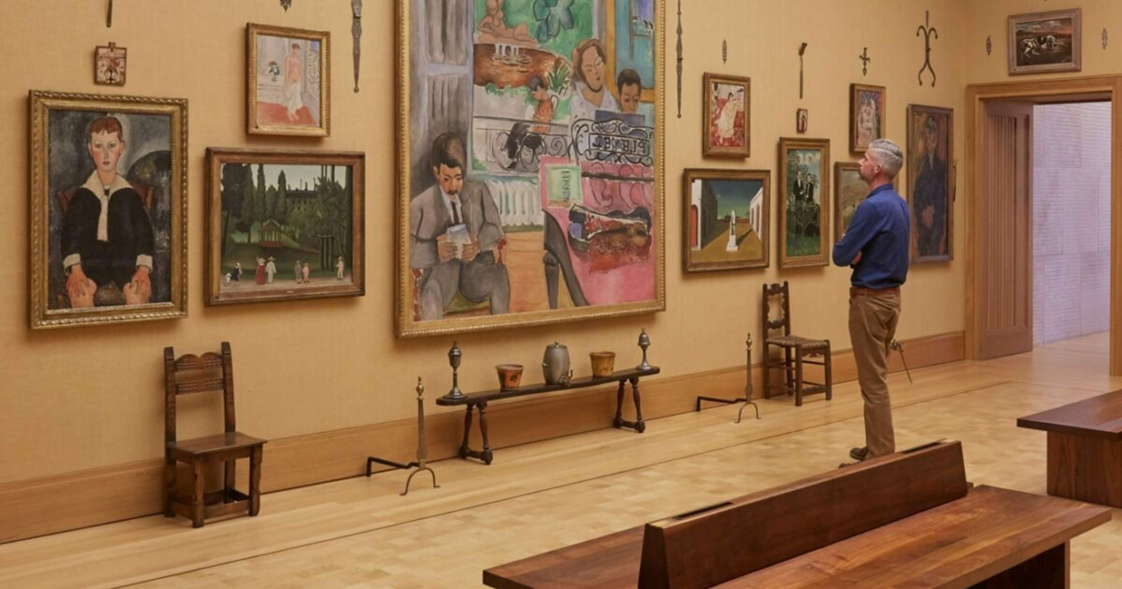 An image of the Barnes Foundation in Philadelphia. A male museum visitor is seen admiring a series of work on the wall, displayed against a yellow background.