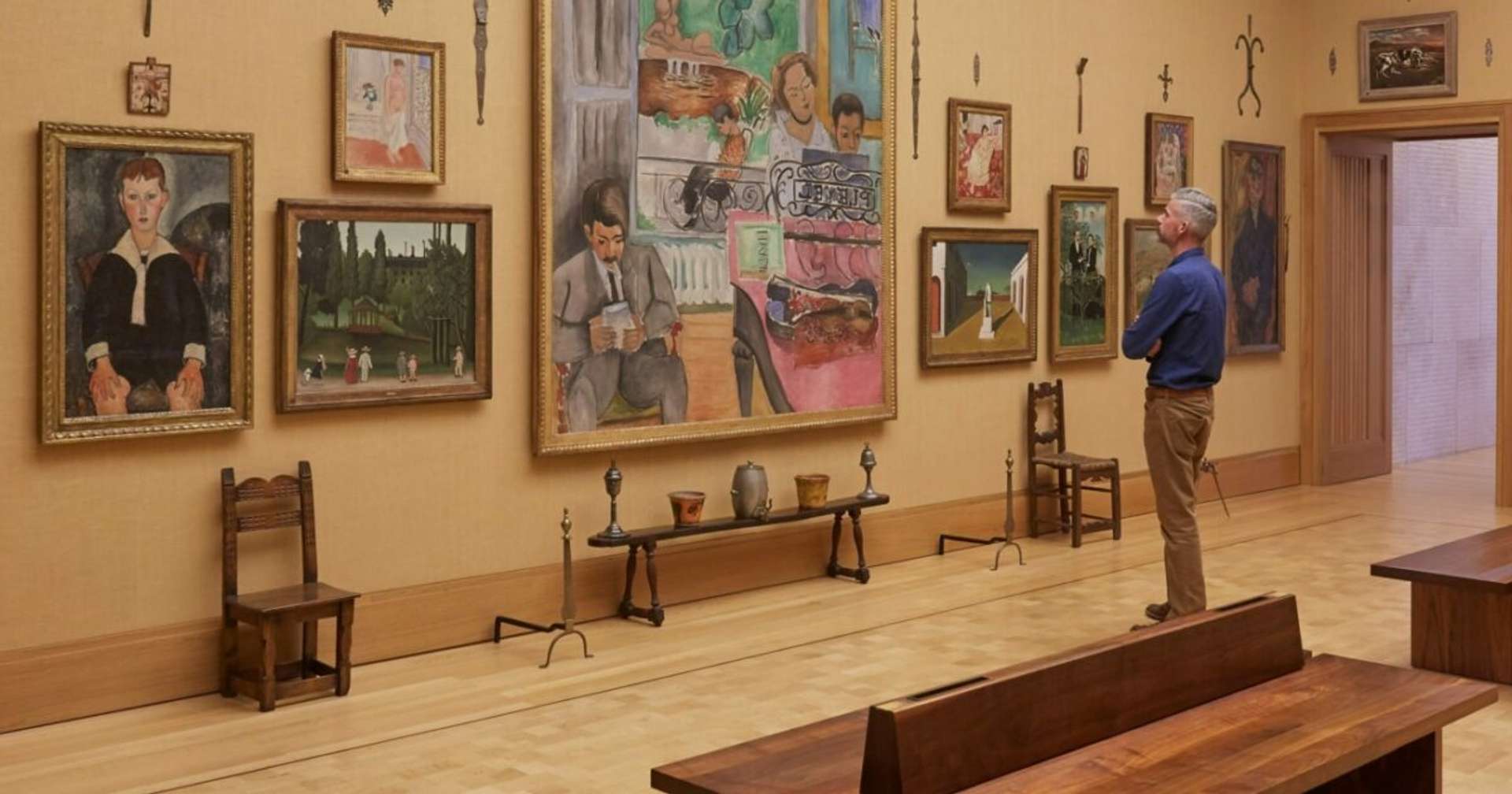 An image of the Barnes Foundation in Philadelphia. A male museum visitor is seen admiring a series of work on the wall, displayed against a yellow background.