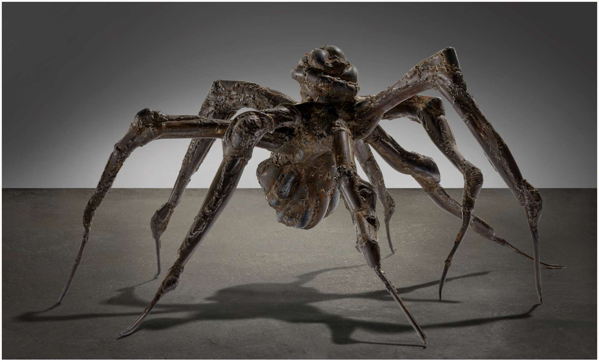 A steel spider sculpture displayed on the ground, featuring a thick body and legs that gradually taper to thin tips. The sculpture exudes a sense of weightlessness, with its body shifting upwards as if in a gaze.