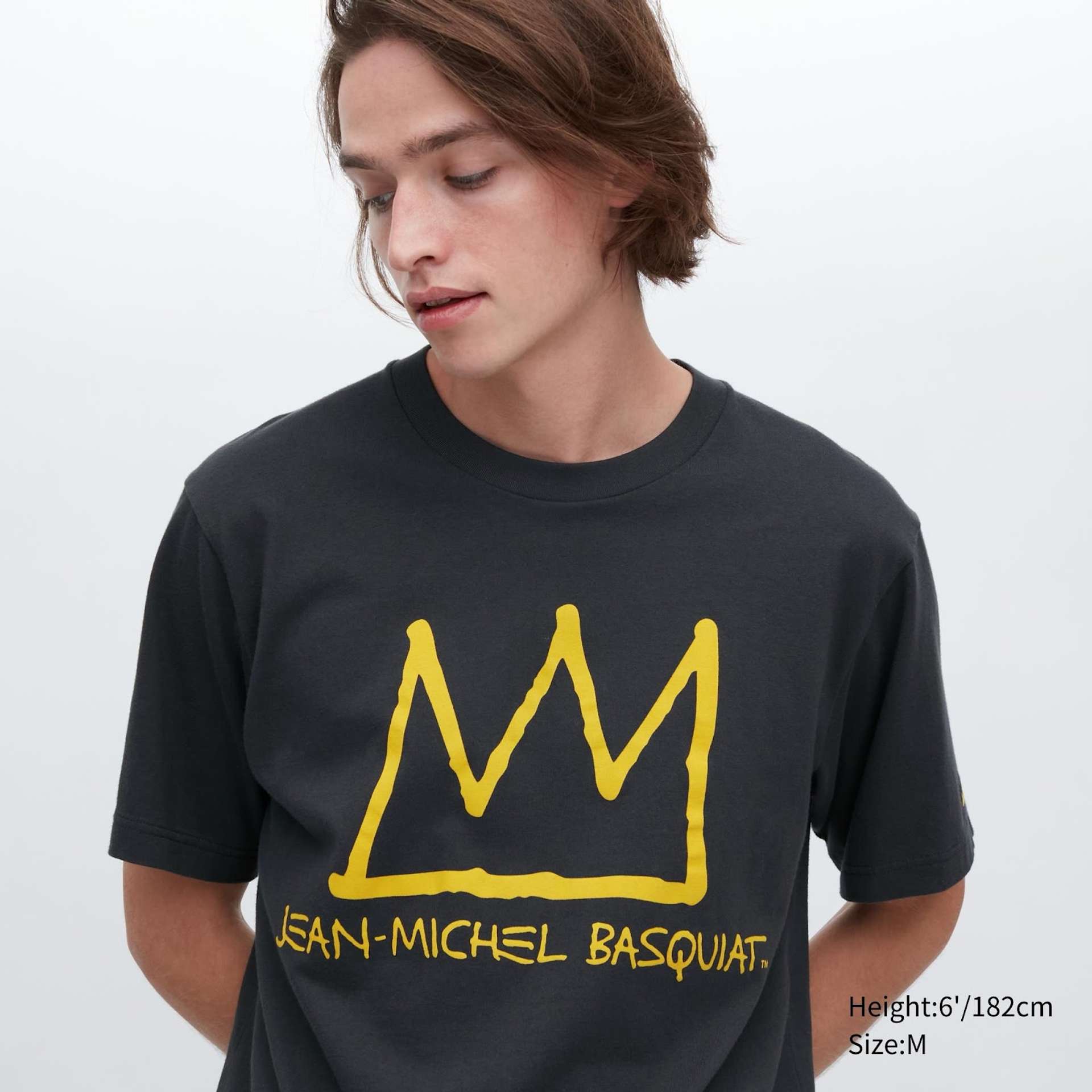An image of a model wearing a grey Uniqlo t-shirt featuring a yellow depiction of Basquiat’s crown motif with the artist’s name underneath.