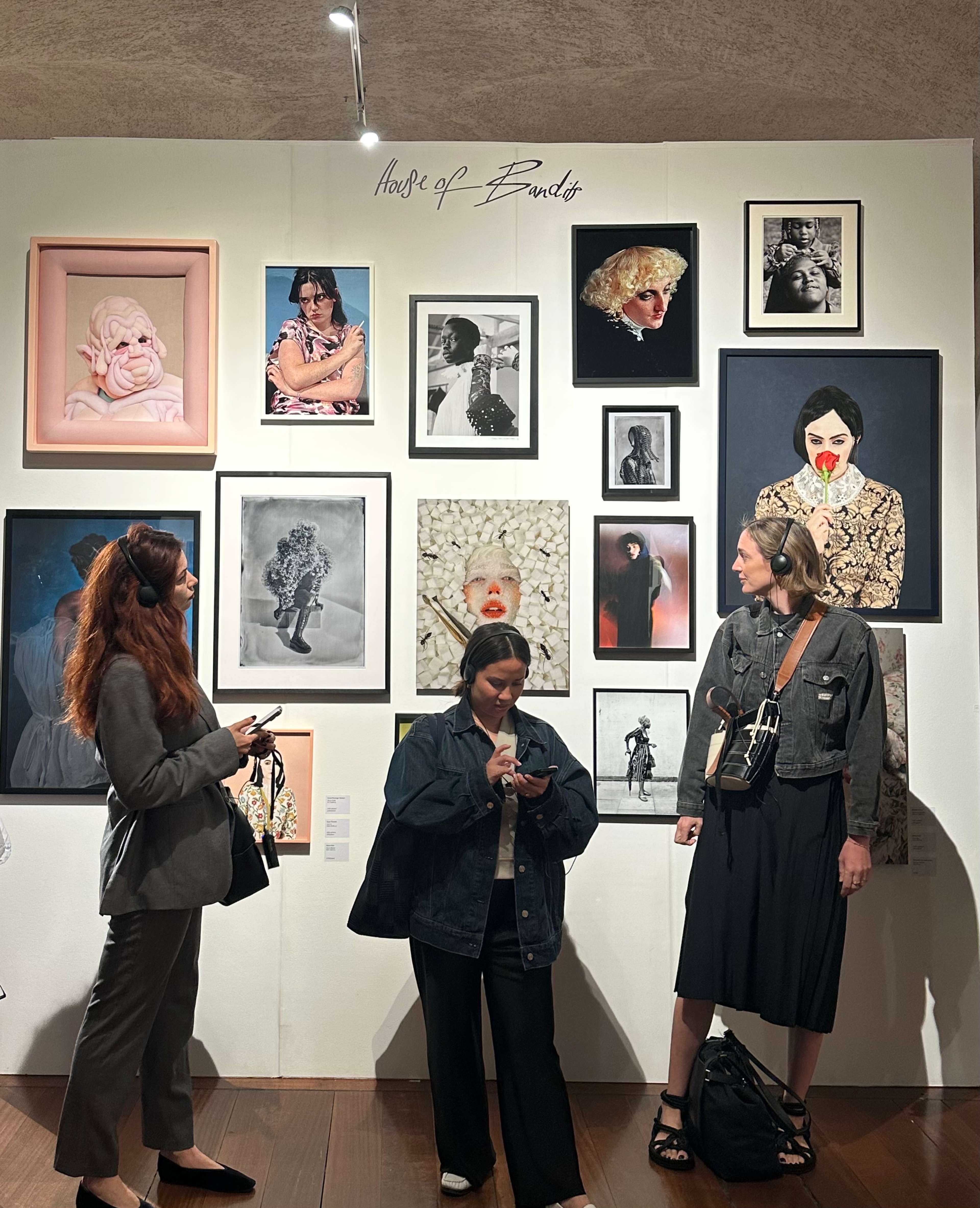 An installation view with three women in front of a wall of artworks.