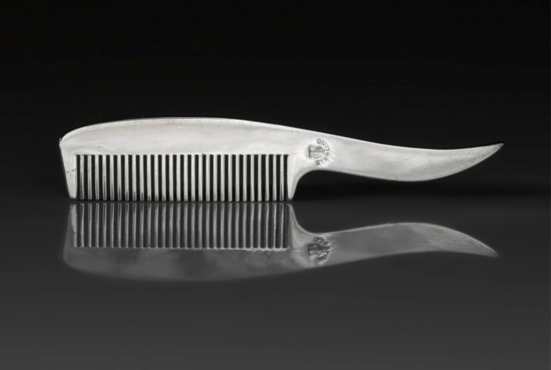 An image of a silver moustache comb by Tiffany & Co against a black background.