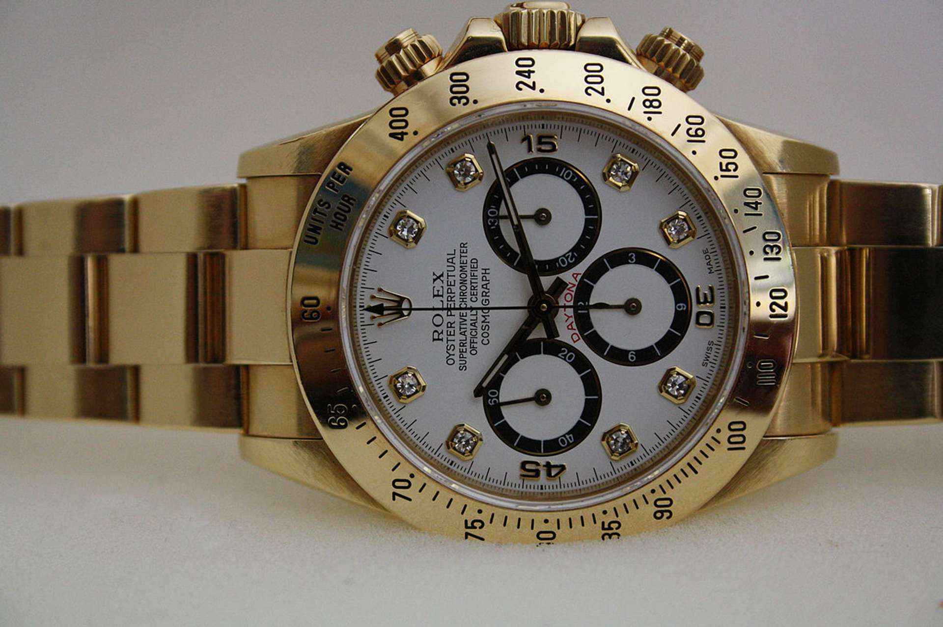 A Rolex Daytona, first launched in 1963. Set against a white background, the watch has a gold metal strap and a white face with three subdials.