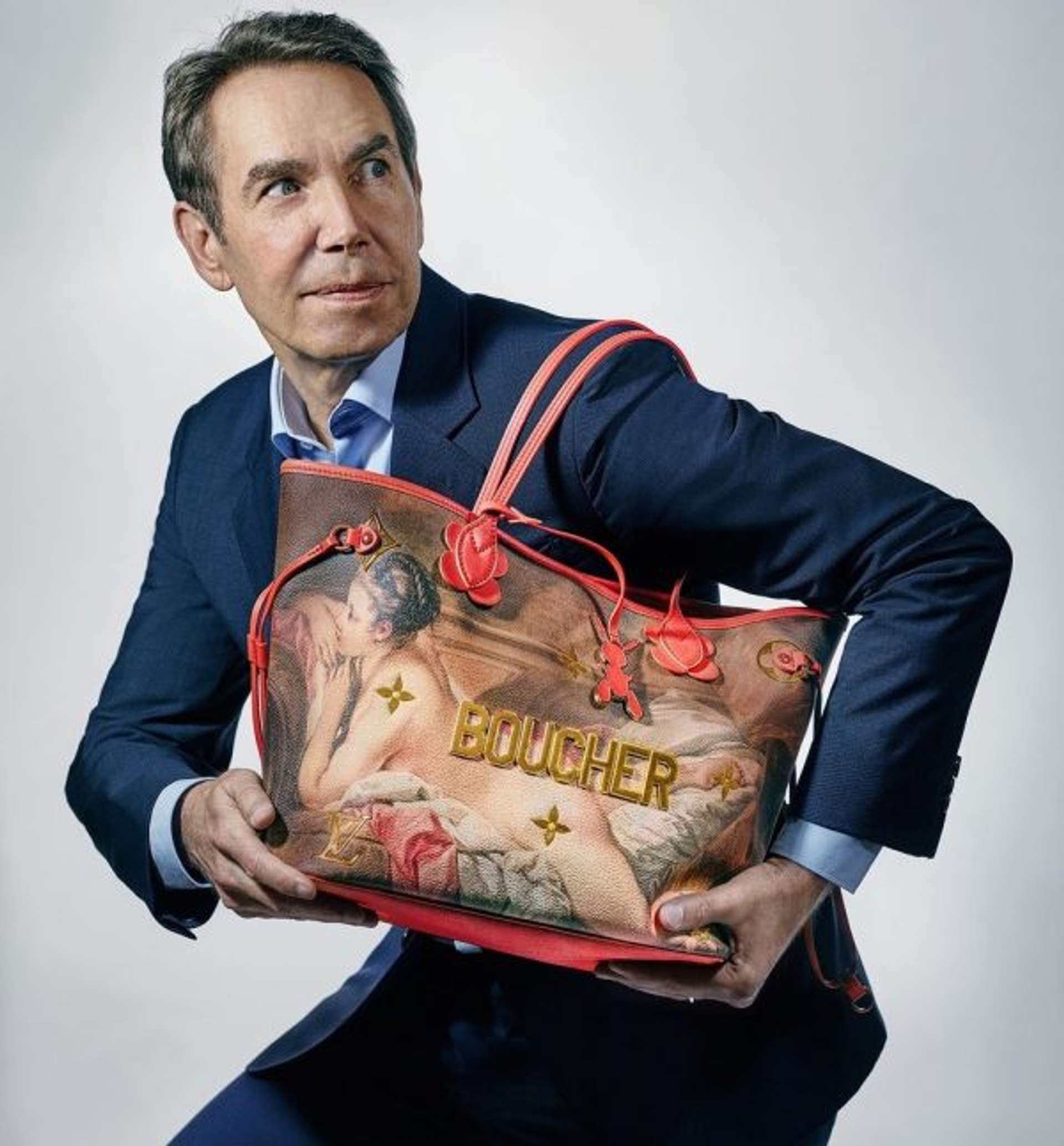 An image of artist Jeff Koons holding one of the bags he designed in collaboration with Louis Vuitton.]