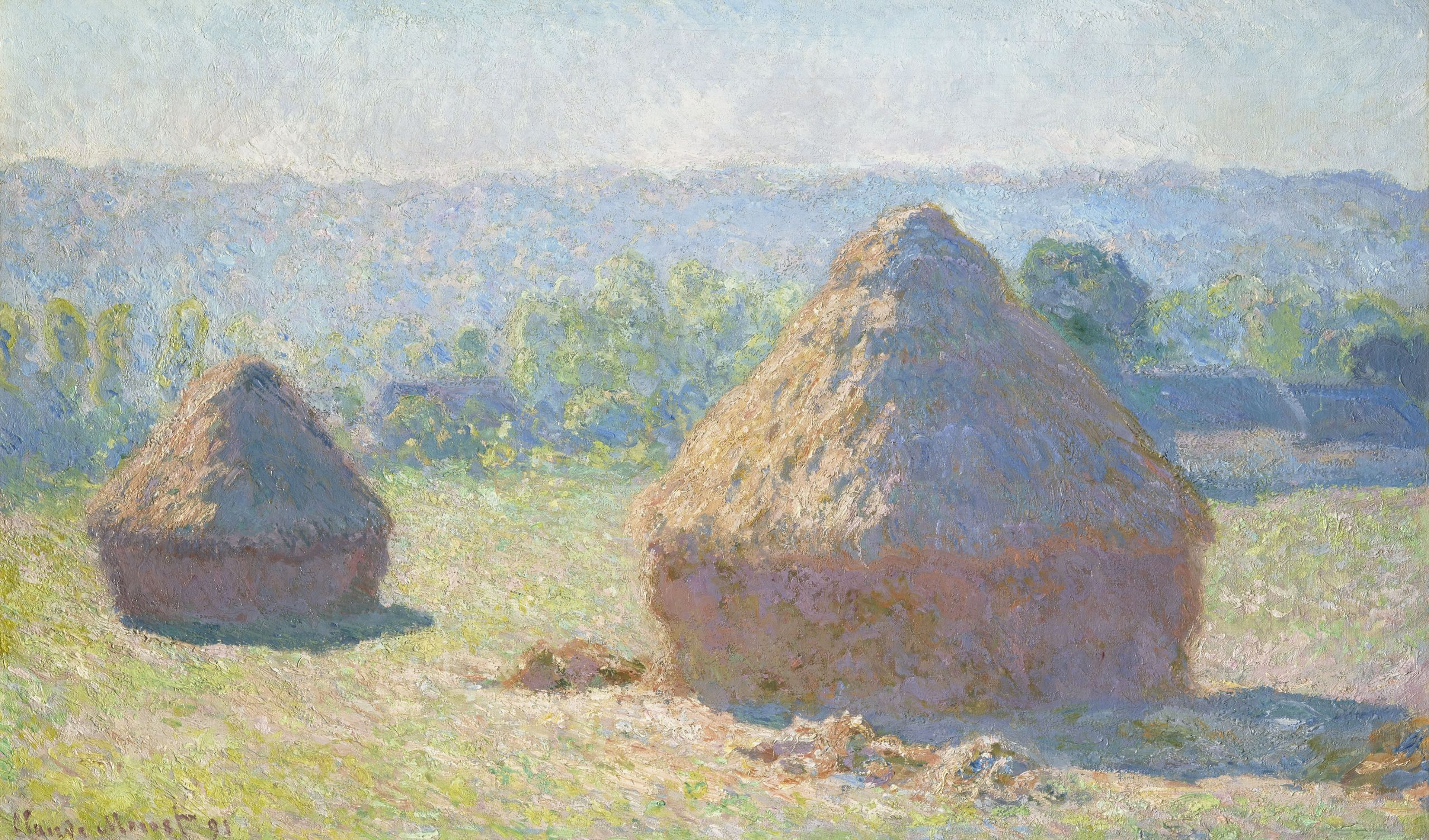 This image shows two large hay stacks on a grassy field, bathed in golden sunlight.