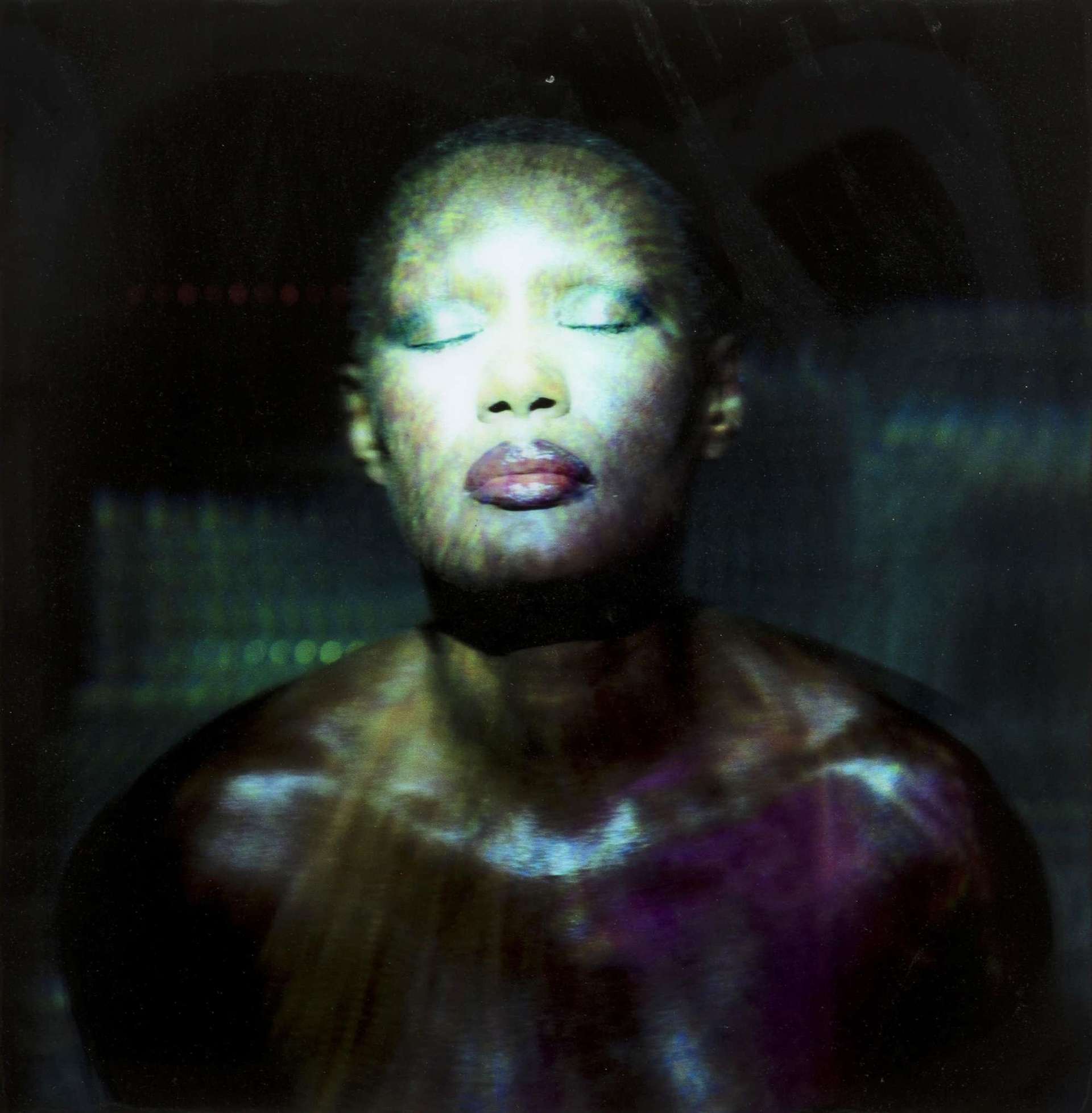 This portrait shows icon Grace Jones, facing up at the camera with her eyes closed. She is illuminated by distorted lights.