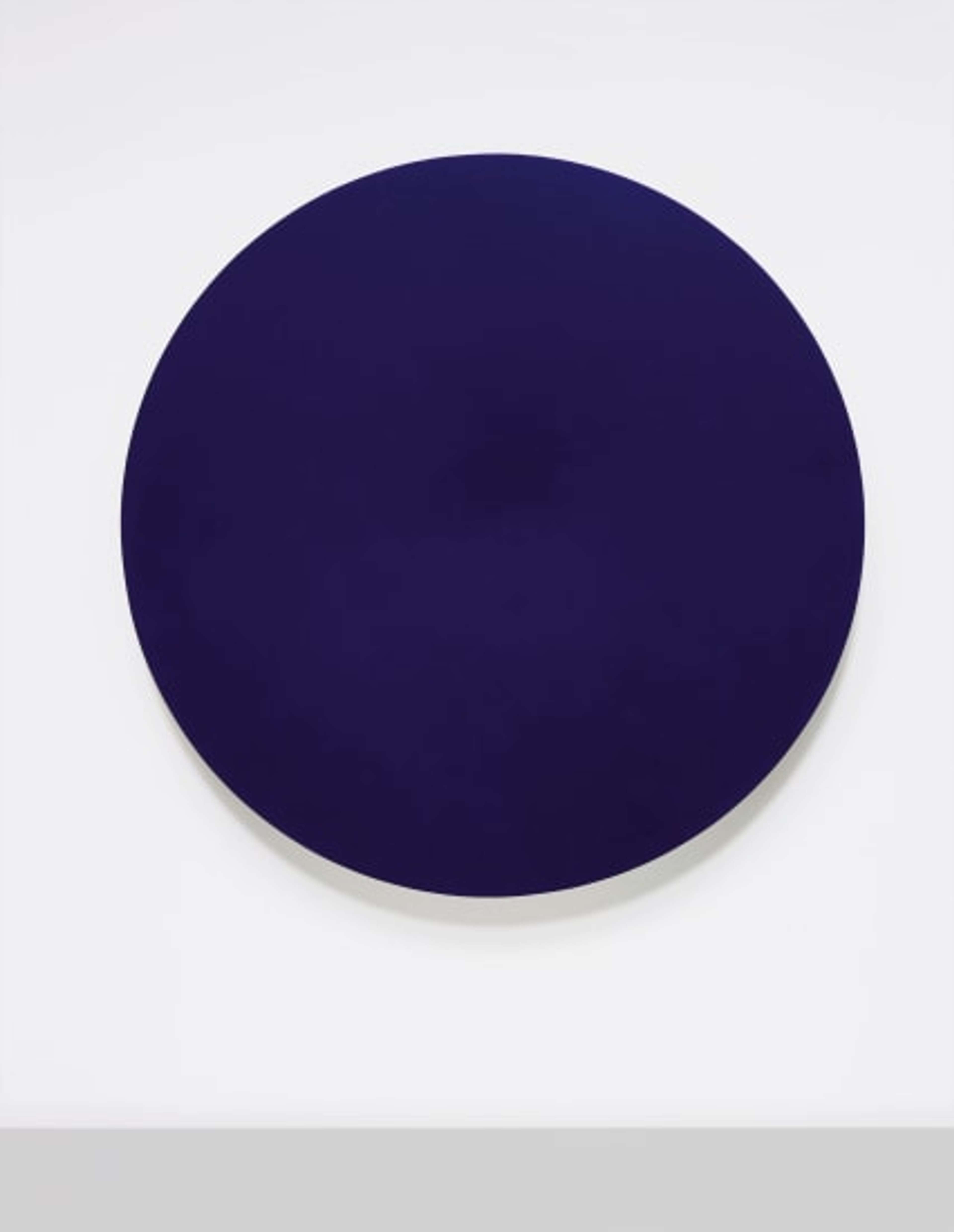 A circular disc covered in dark blue, matte pigment. It has a soft-looking surface and seems to absorb the light around it.