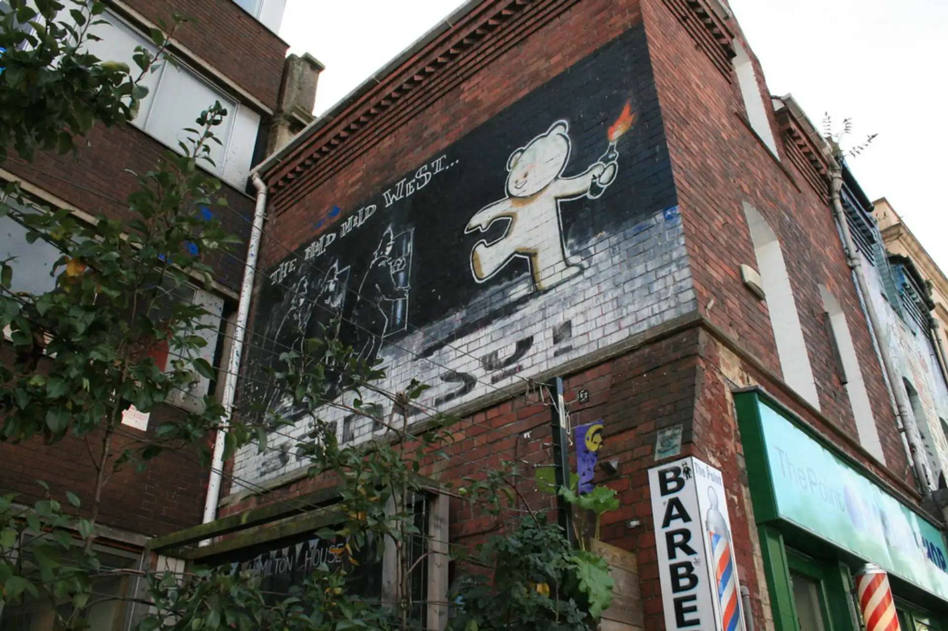 A photograph of Banksy's Mild Mild West in-situ graffiti work, depicting a teddy bear throwing a petrol bomb at three riot policemen.