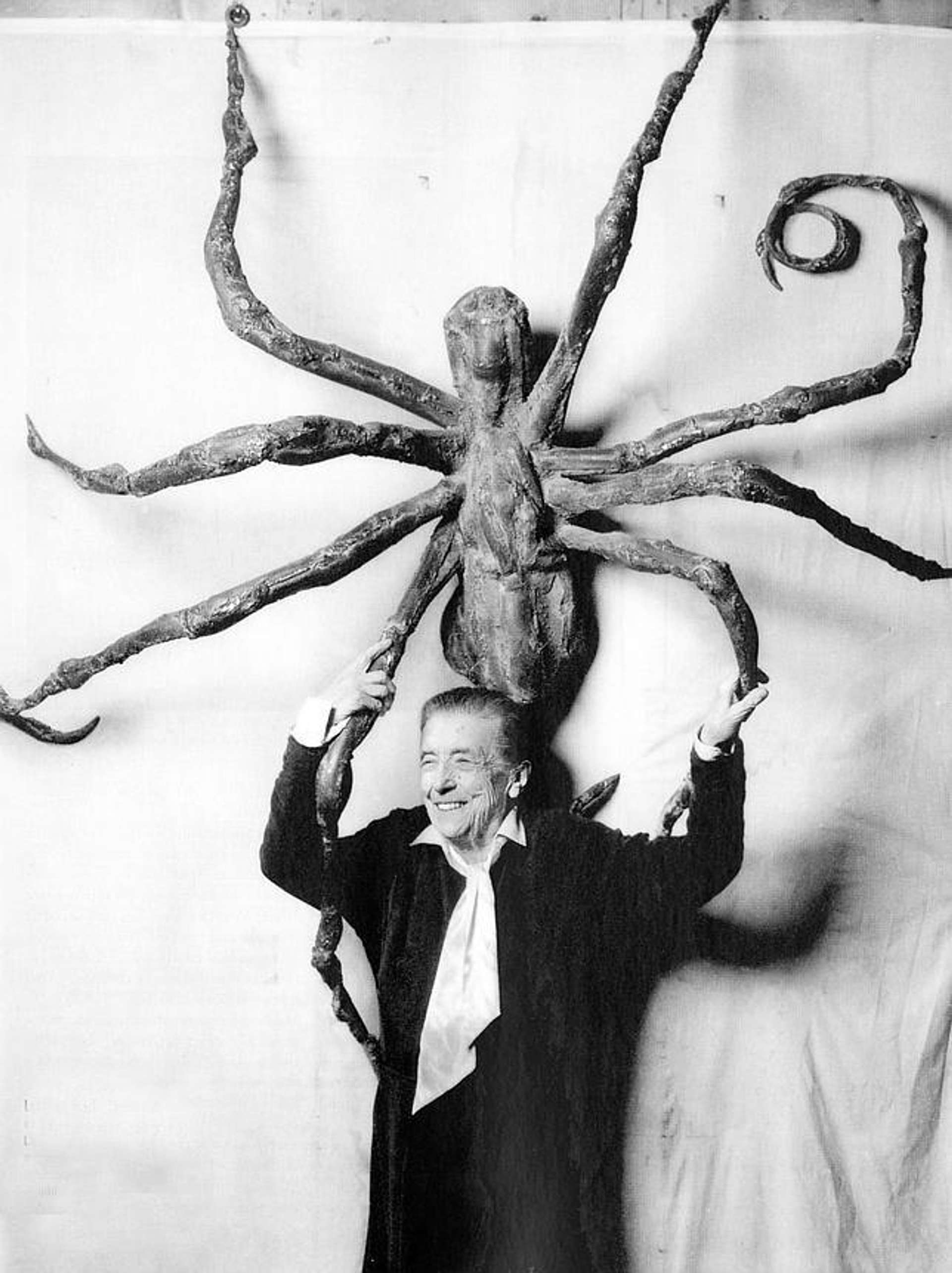 Black and white photograph of Louise Bourgeois standing beneath a large spider sculpture