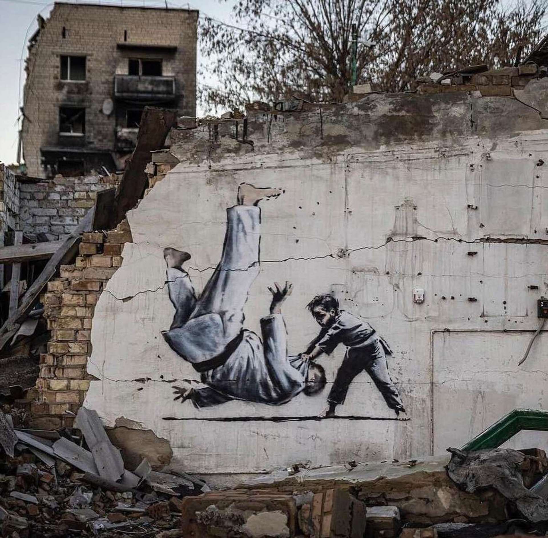This mural by Banksy is done on the side of a semi ruined building. It shows a young girl knocking out a large man using Judo moves.