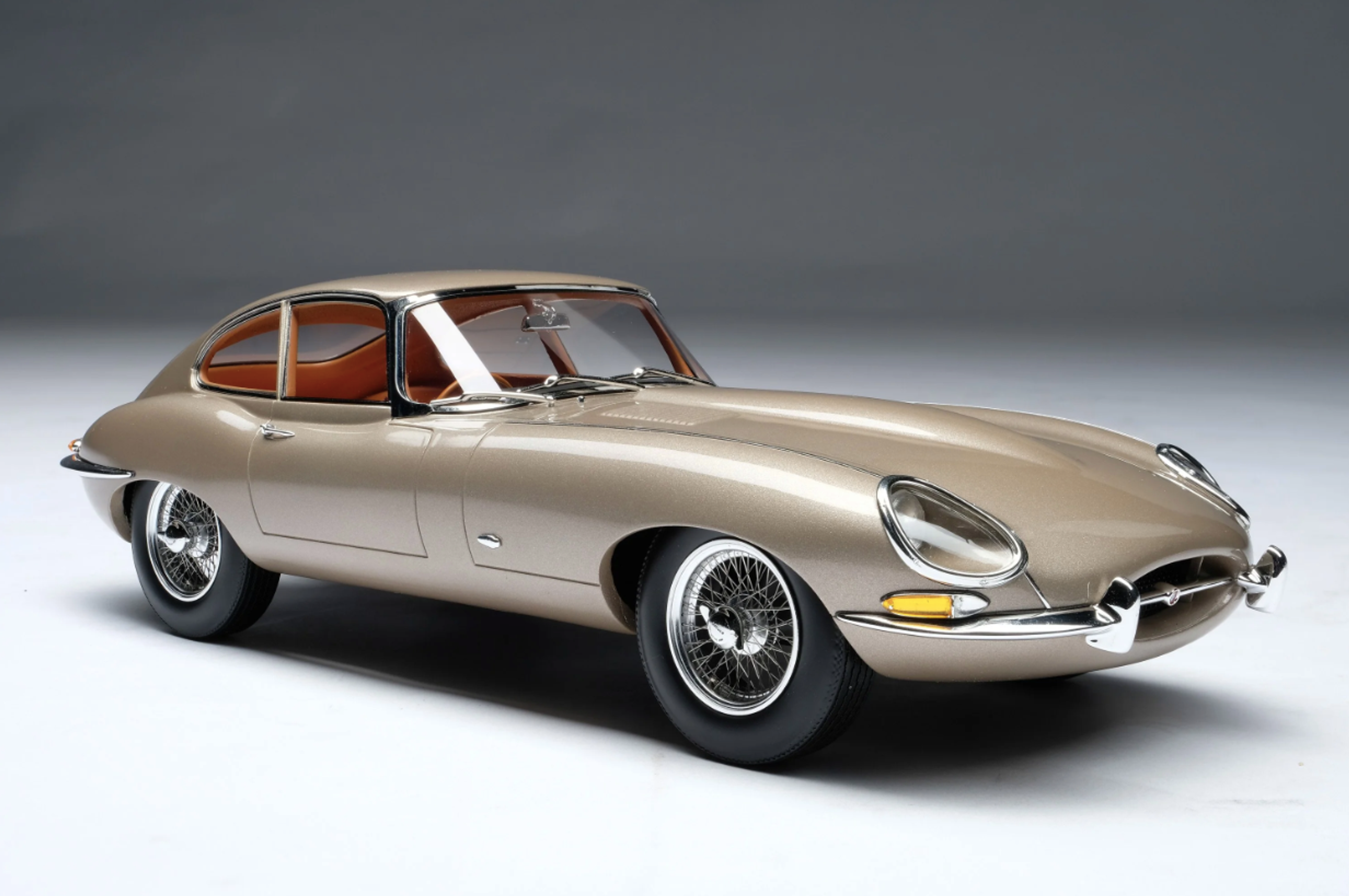 A champagne coloured Jaguar E-type Couple from 196, set against a plain studio background.