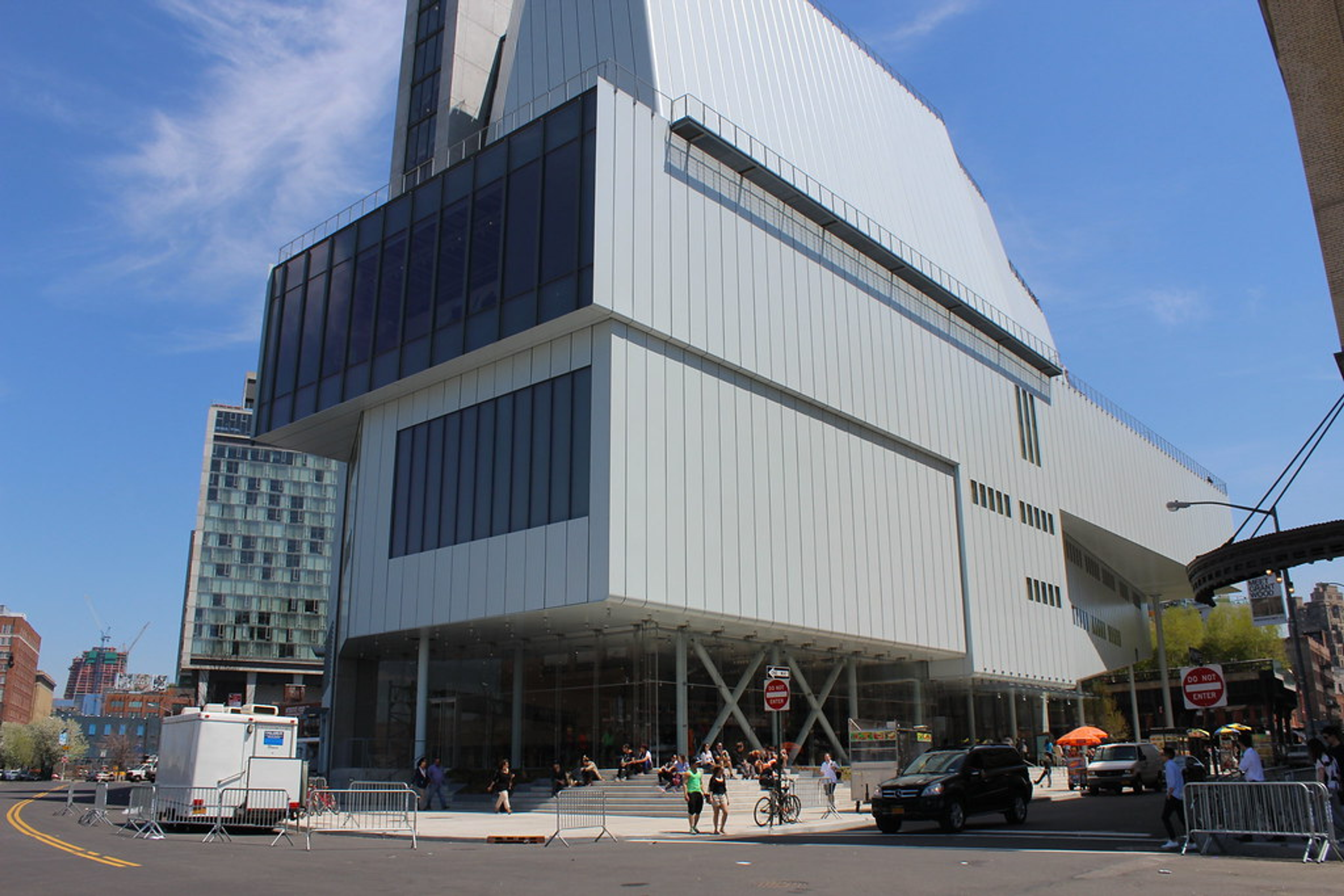 An outdoor image of the facade of the Whitney Museum, a modernist looking building against a blue sky.