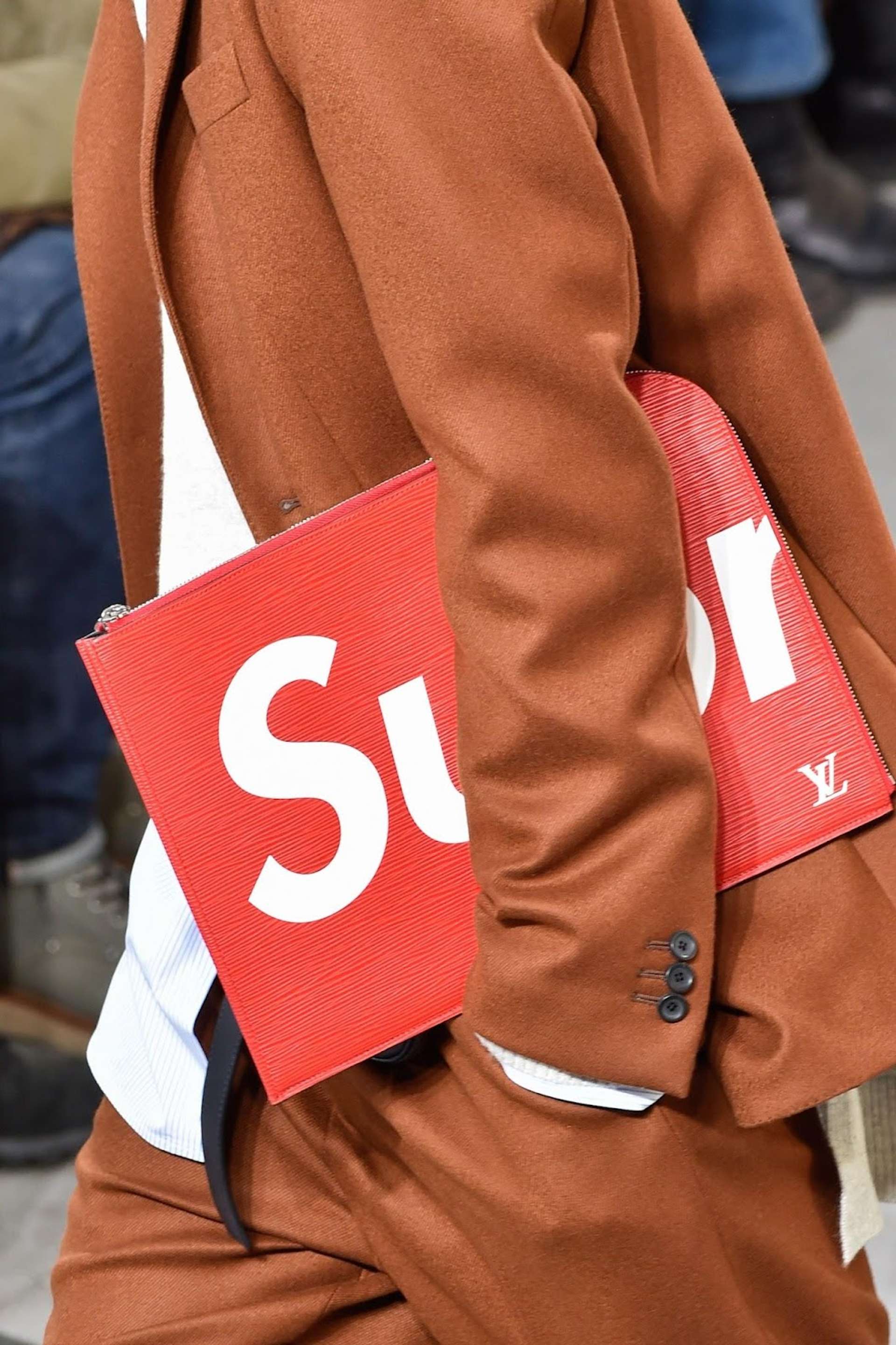 An image of a model wearing a suit while holding one of the bags that brand Supreme designed in collaboration with Louis Vuitton.
