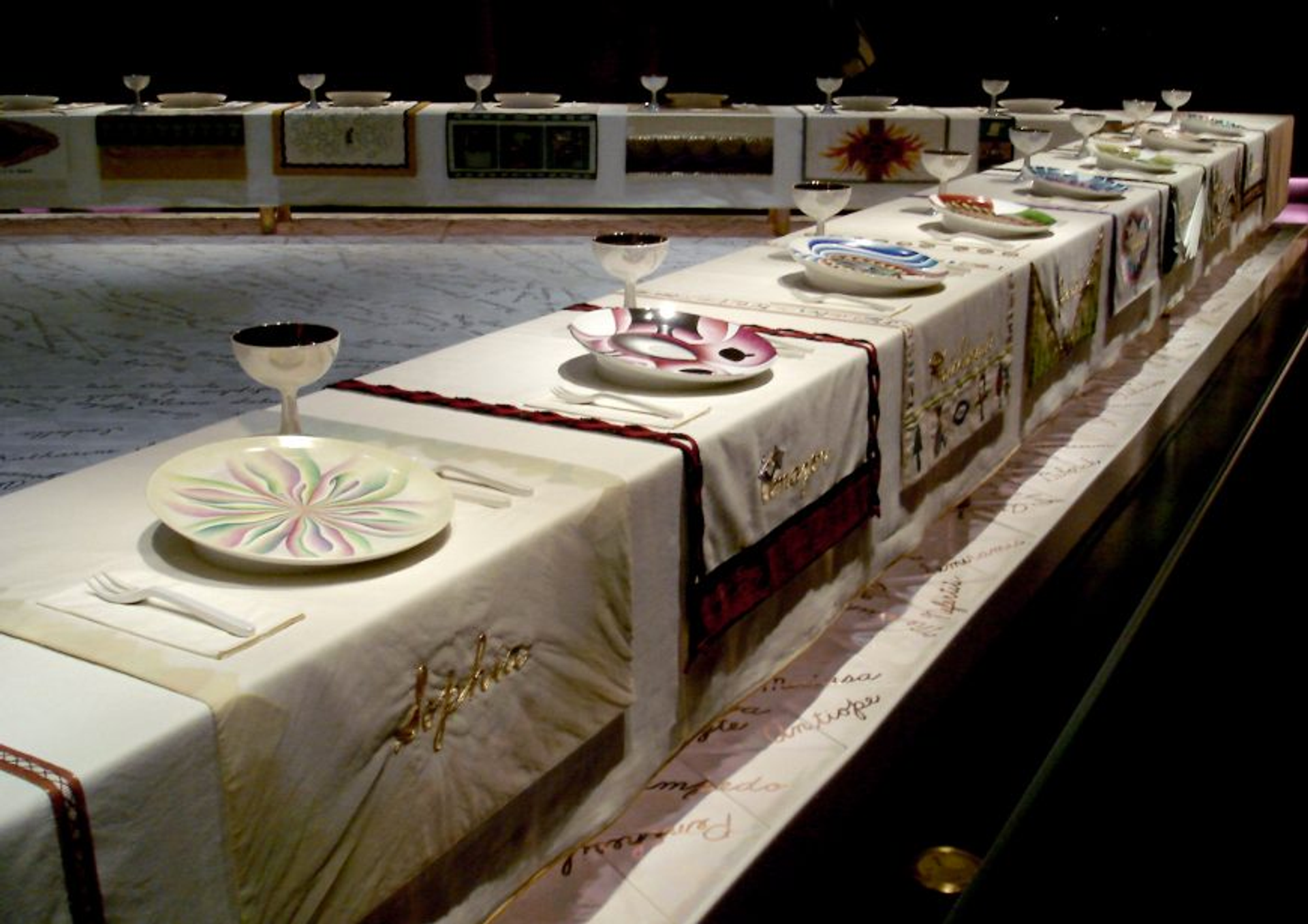 A photograph of Louise Bourgeois’ The Dinner Party installation. A view of a triangular-shaped dining table with ornate and decorative place settings.