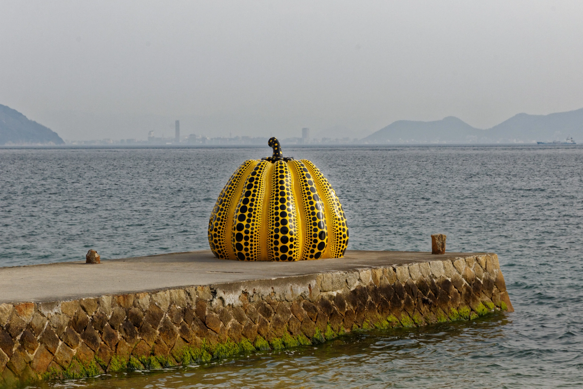 One of Yayoi Kusama's giant pumpkin sculptures is depicted against a harbour scene.