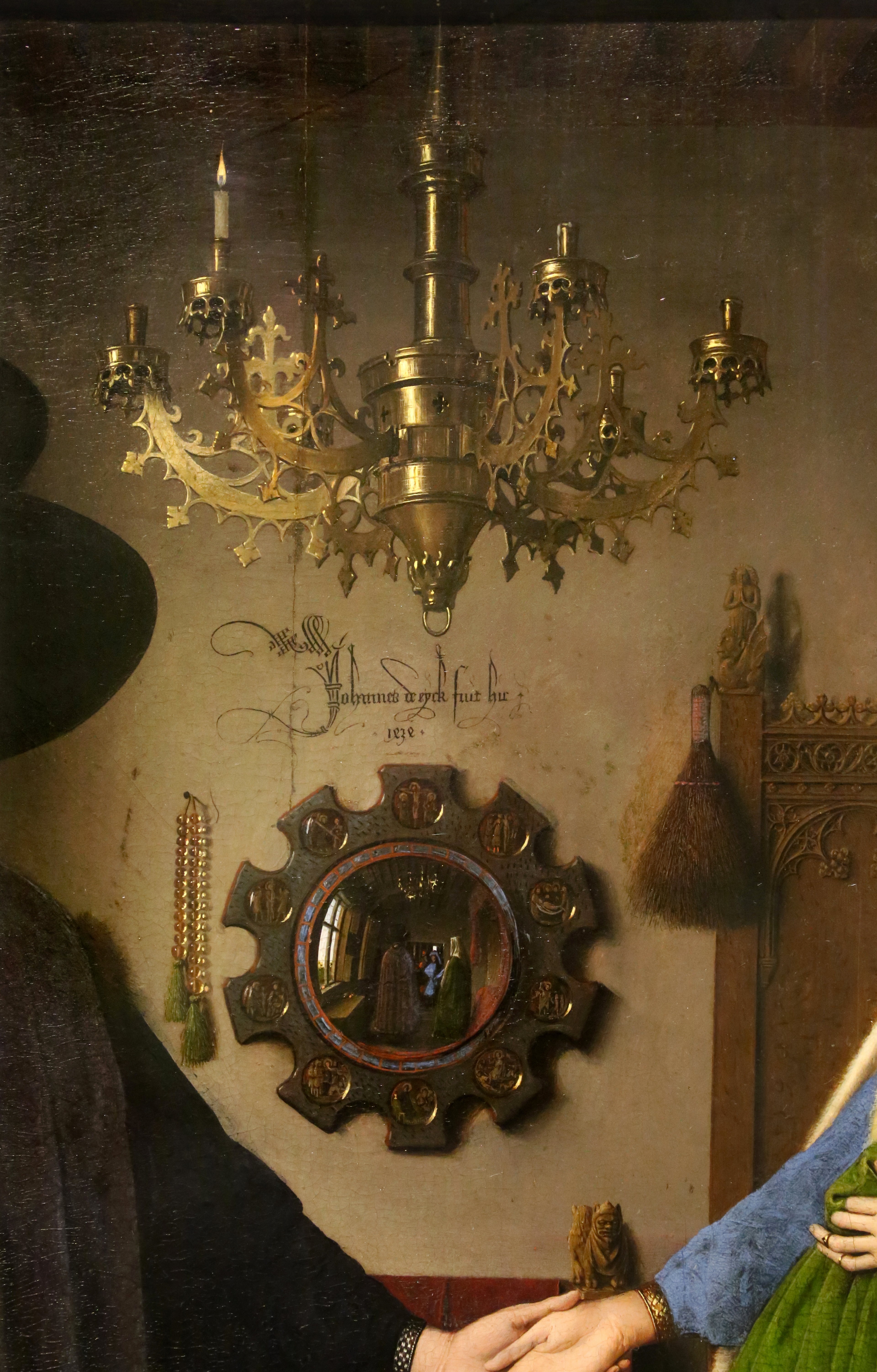 This image shows a closeup of the Arnolfini Portrait, showing a detailed chandelier and a mirror that is reflecting the entirety of the room.