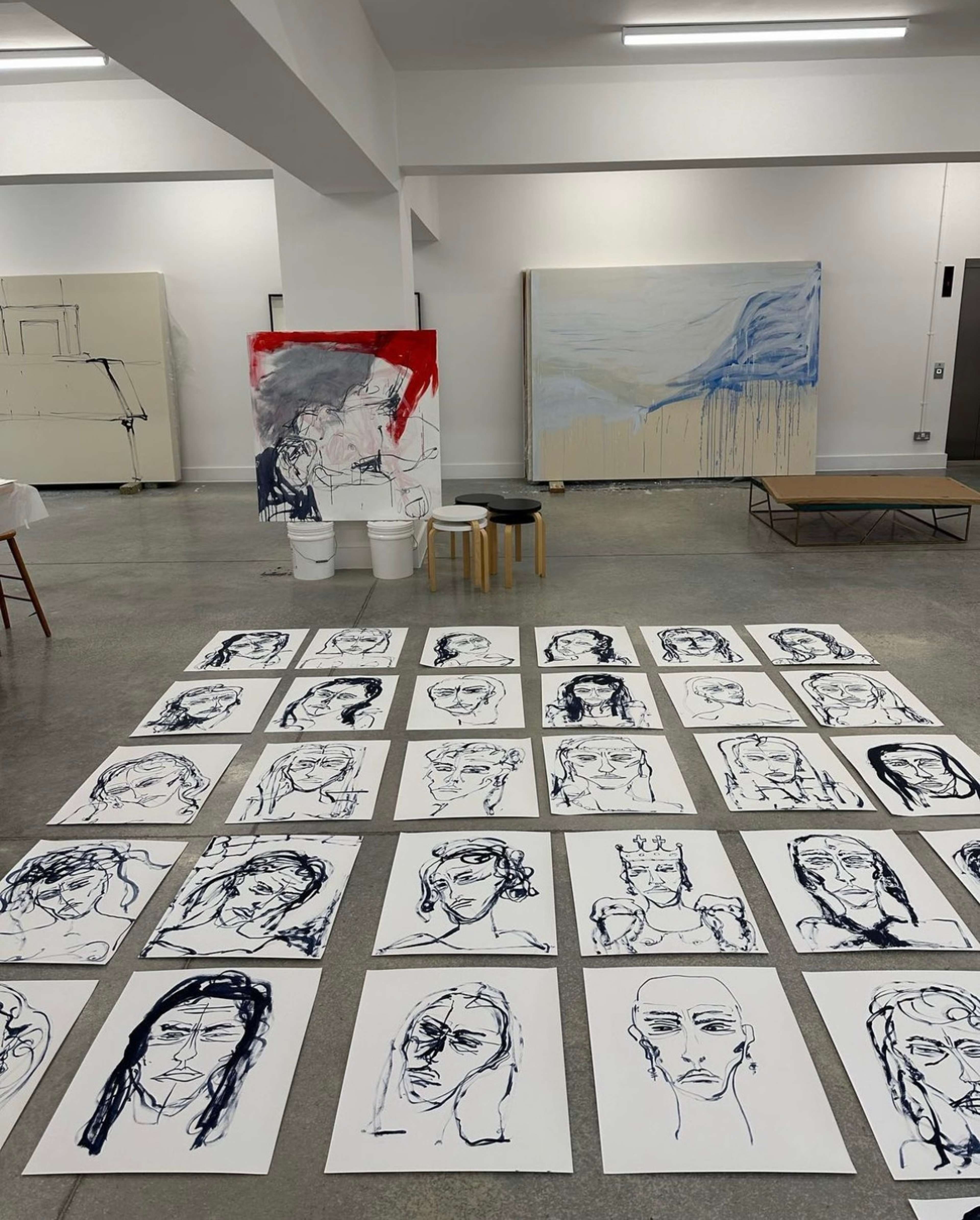 A photograph of Tracey Emin's studio, capturing the preliminary drawings of her female portraits for The Doors at the National Portrait Gallery in London. The blue ink drawings are spread across the floor in the order Emin planned for the execution of the bronze doors.