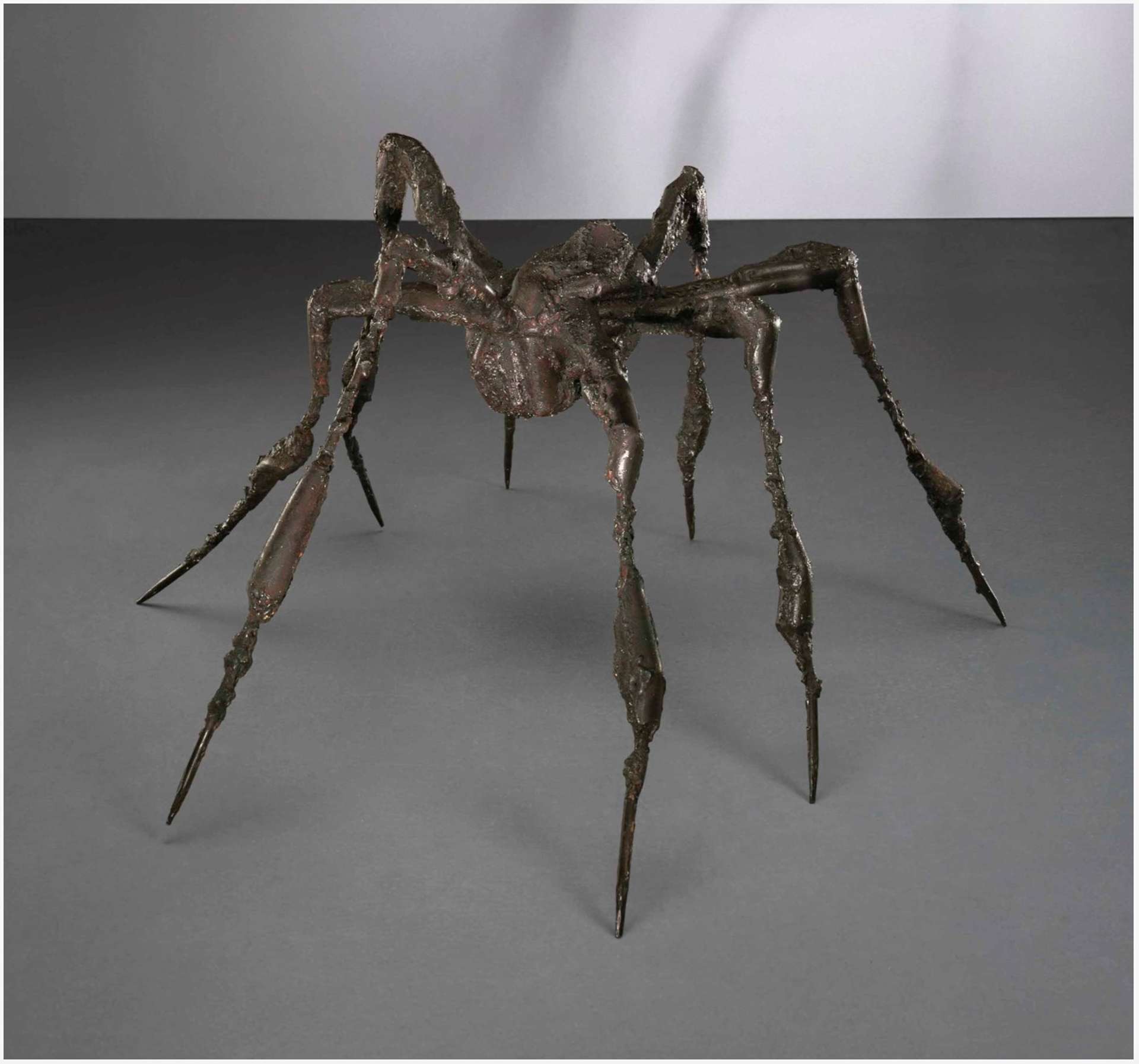 A steel spider sculpture with a robust body resting on the ground, its eight sturdy limbs balanced delicately on their tips, creating a static and stable pose.