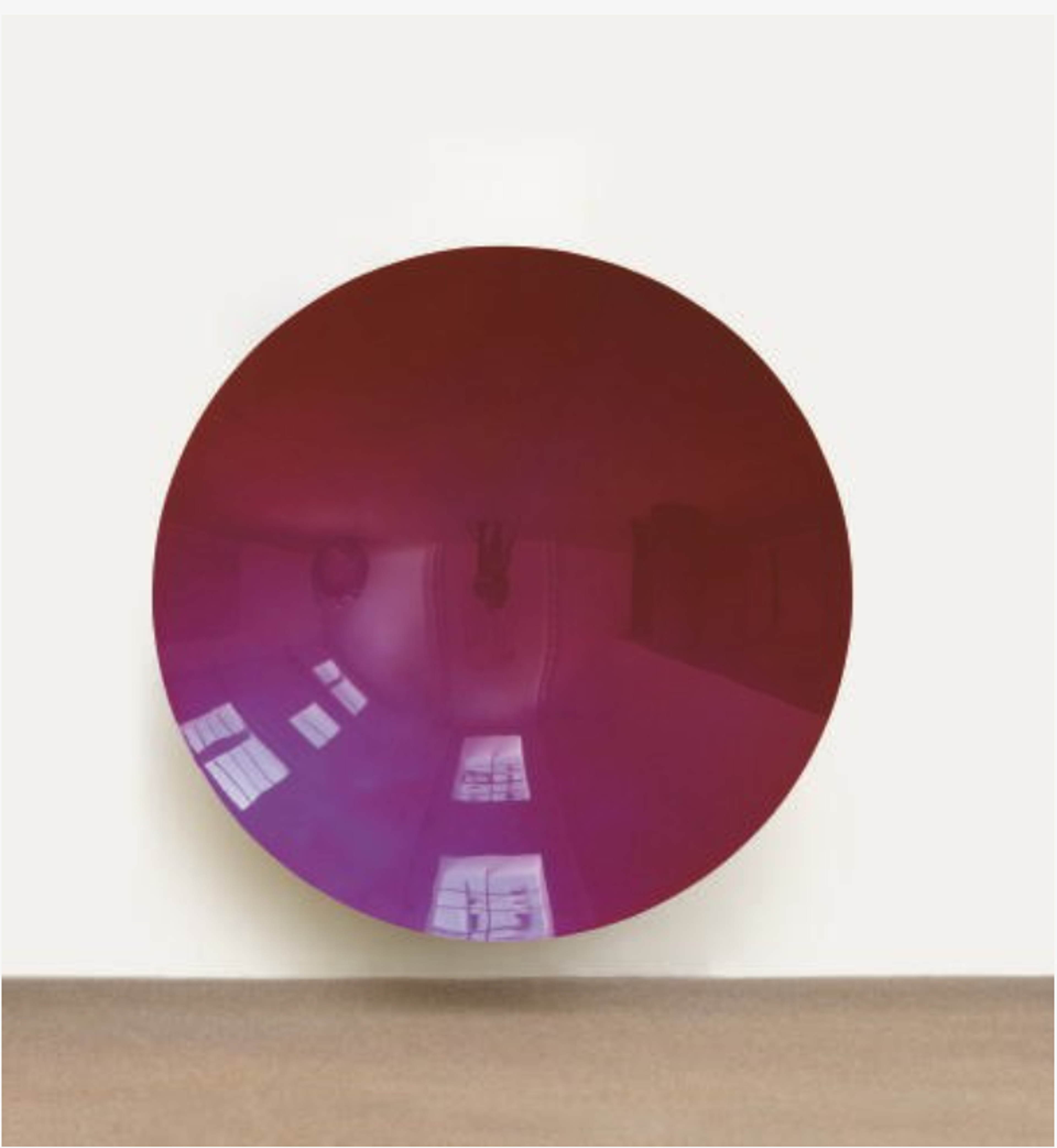 A circular concave red aluminum disc with highly polished reflective surface. The reflection on the disc shows a distorted, inverted gallery space.