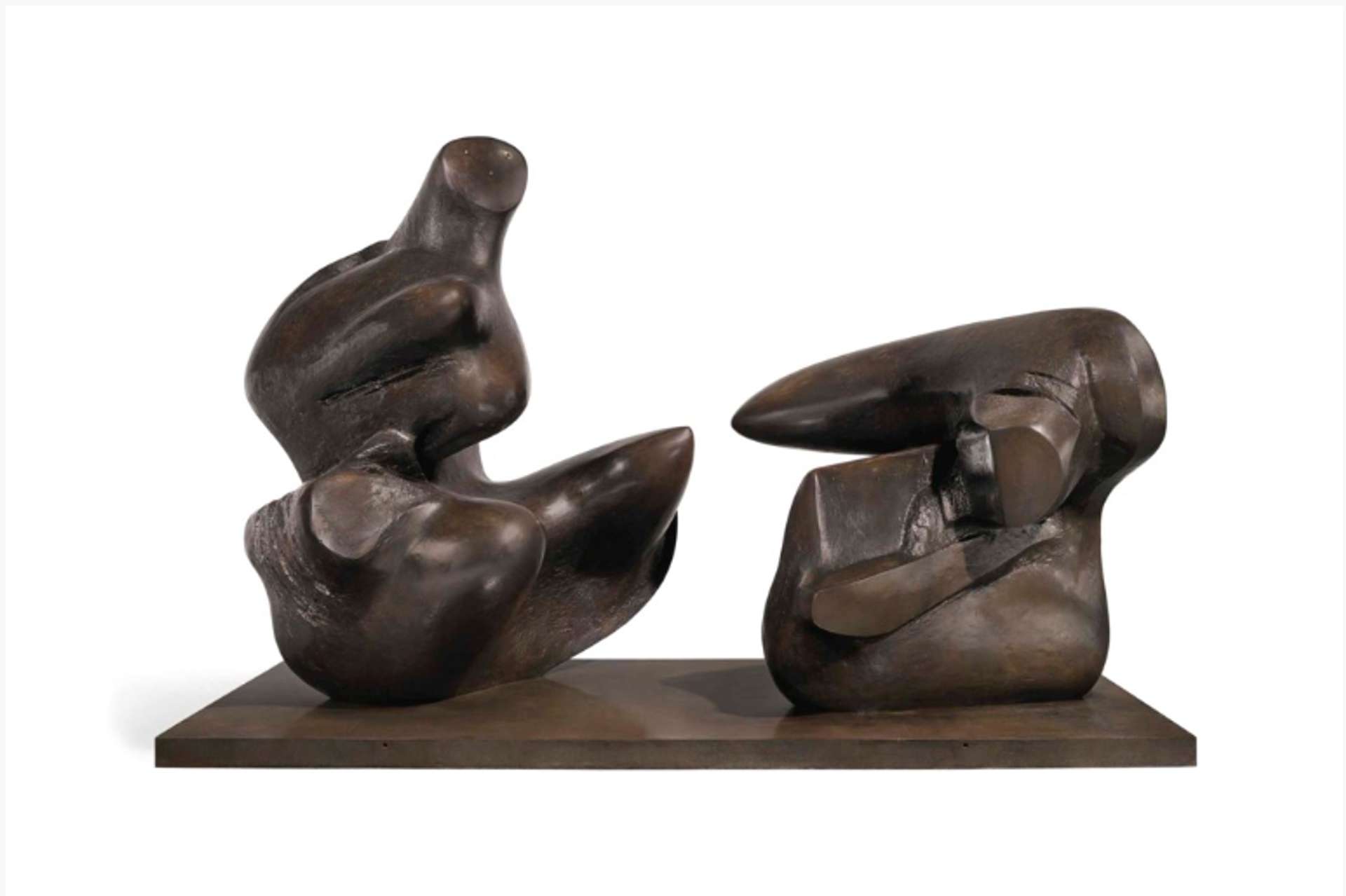 A bronze cast sculpture by Henry Moore portraying a biomorphic reclining figure through two distinct and separated fragments. One fragment demonstrates vertical protrusion, skillfully depicting a balanced composition from its base. The other fragment assumes a geometric form, standing at half the height of its counterpart. Both fragments are positioned on a bronze plinth.