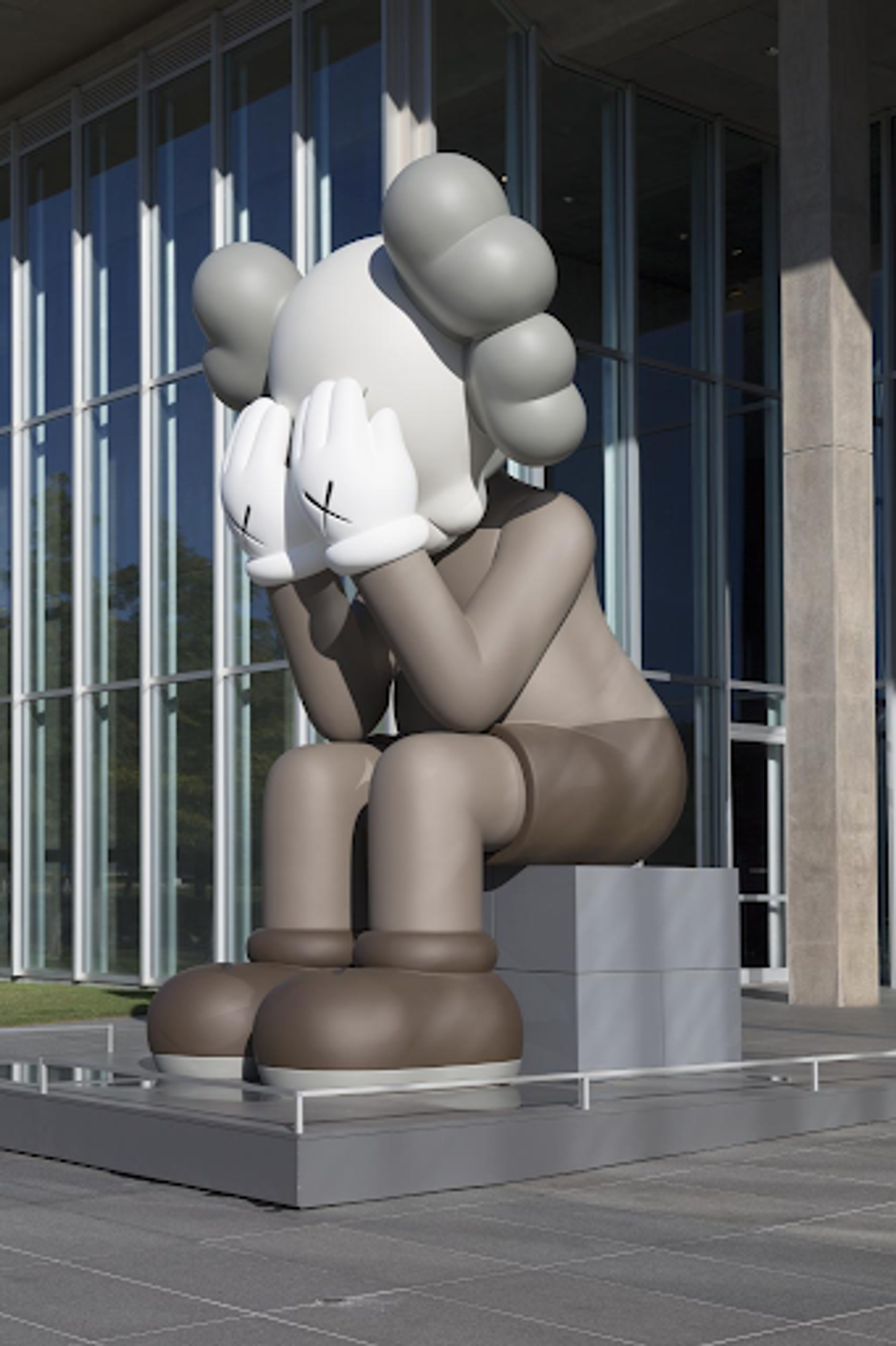 KAWS’ Companion (Passing Through) sculpture. Massive cartoon like character sitting with its elbows on its knees, and face buried into its palms