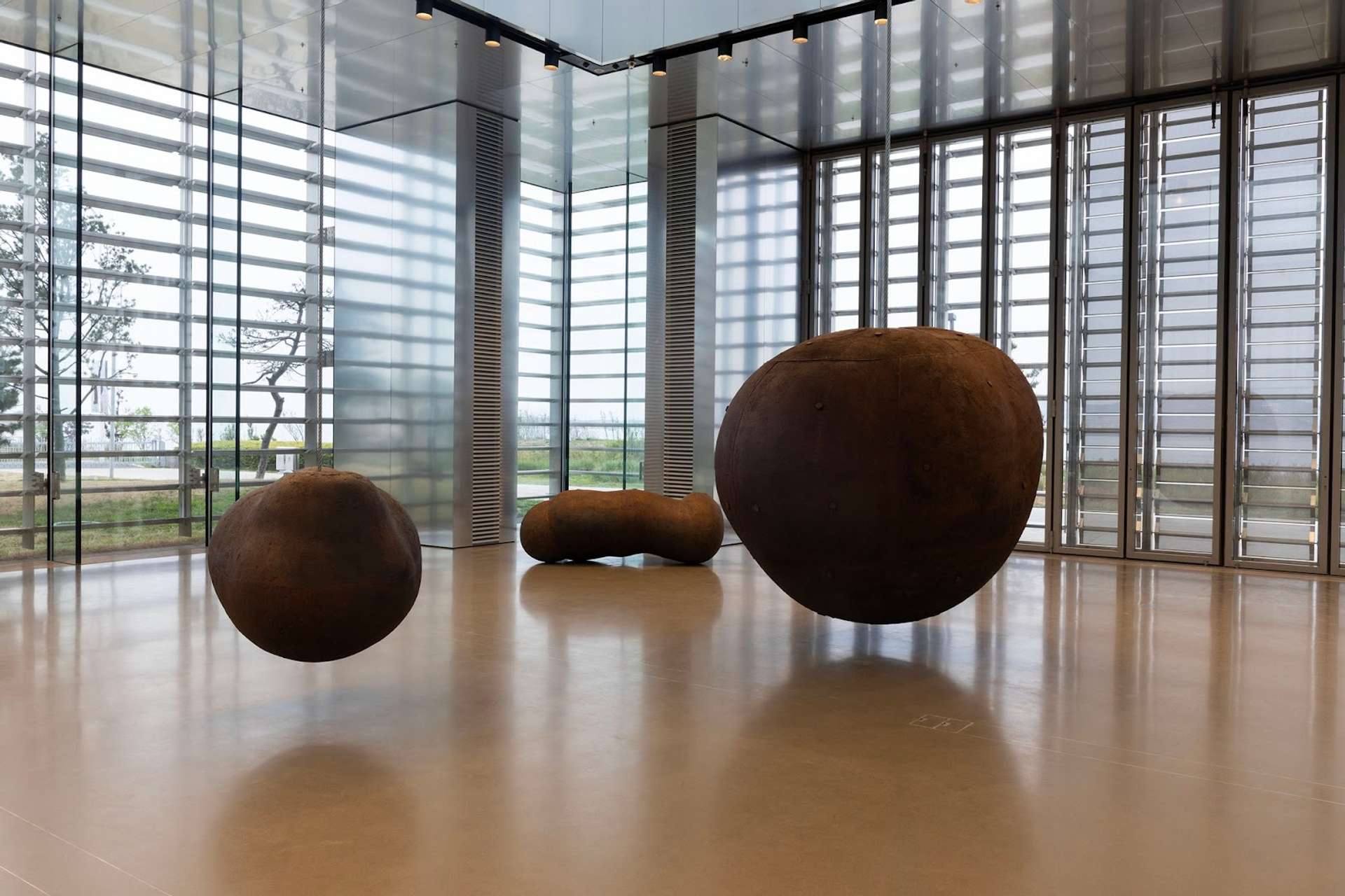 An image of the exhibition Living Time by Antony Gormley. It shows a large room, with glass windows, in which iron-like spheres seem to fluctuate.